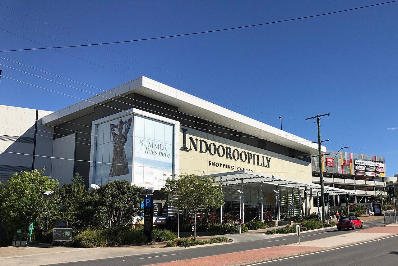 Indooroopilly Shopping Centre exterior under a clear blue sky. Beige and white facade with store signage.