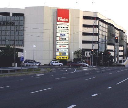Carindale Westfield shopping center exterior with signs for various stores. Cars on road and in parking.