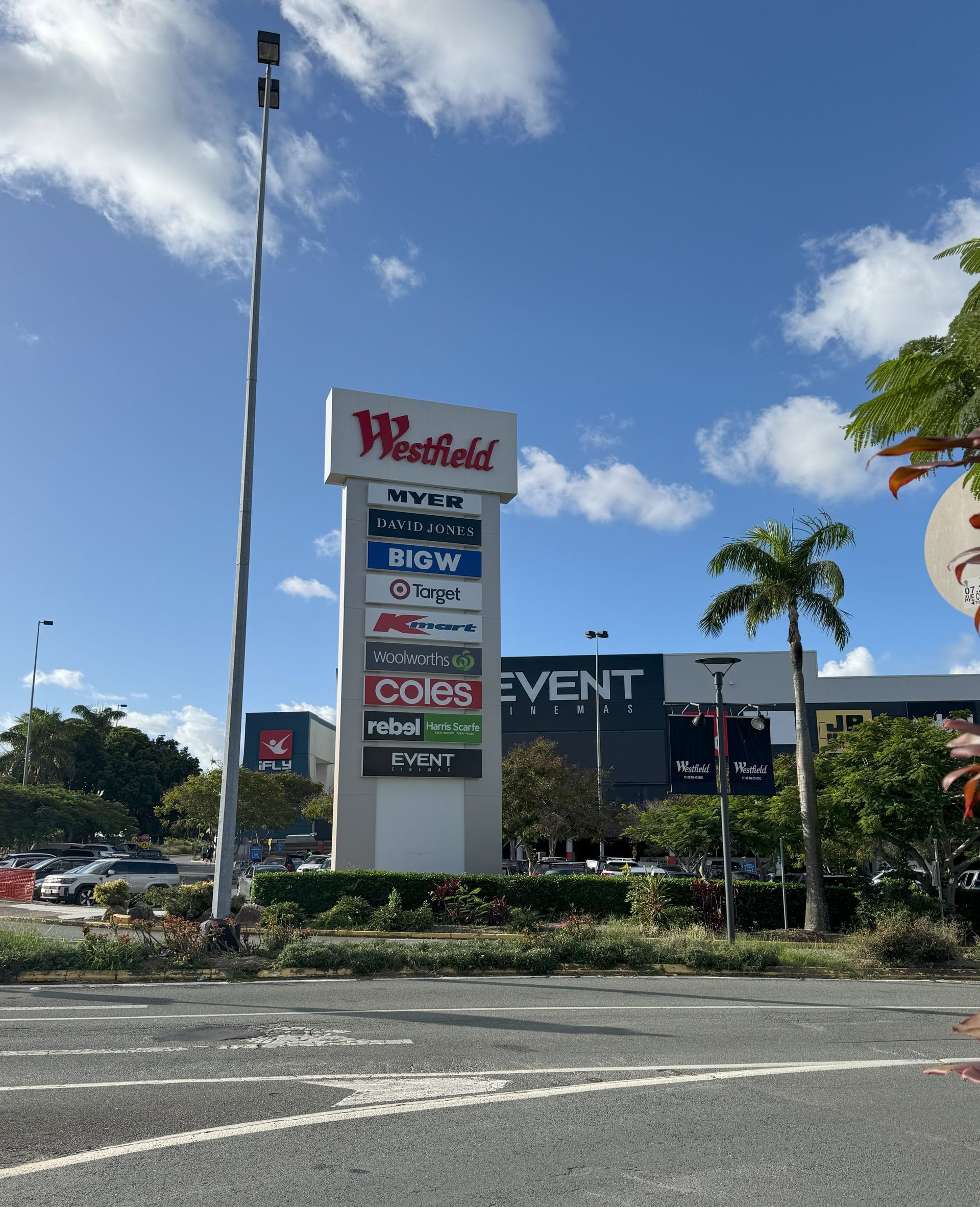 Chermisde Westfield shopping center sign with store logos, blue sky, palm tree, and parking lot.