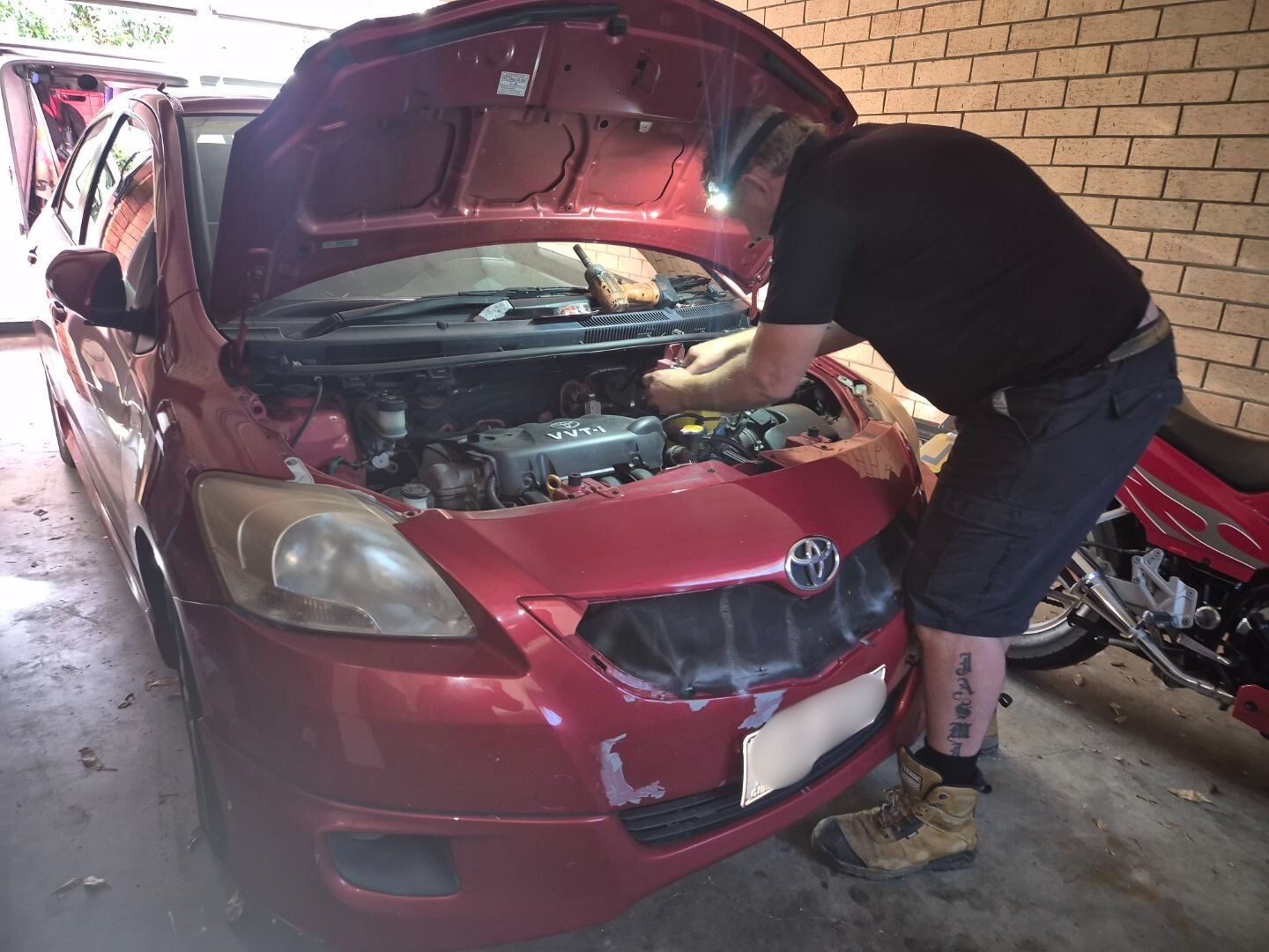 White Toyota Land Cruiser with open hood being worked on, hangar with plane in background.