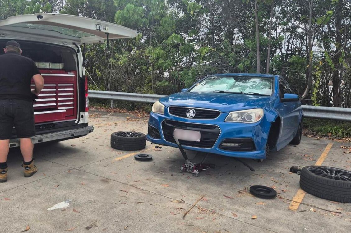 Black car with open hood next to a white van with open back, revealing a red tool chest. Outdoors.