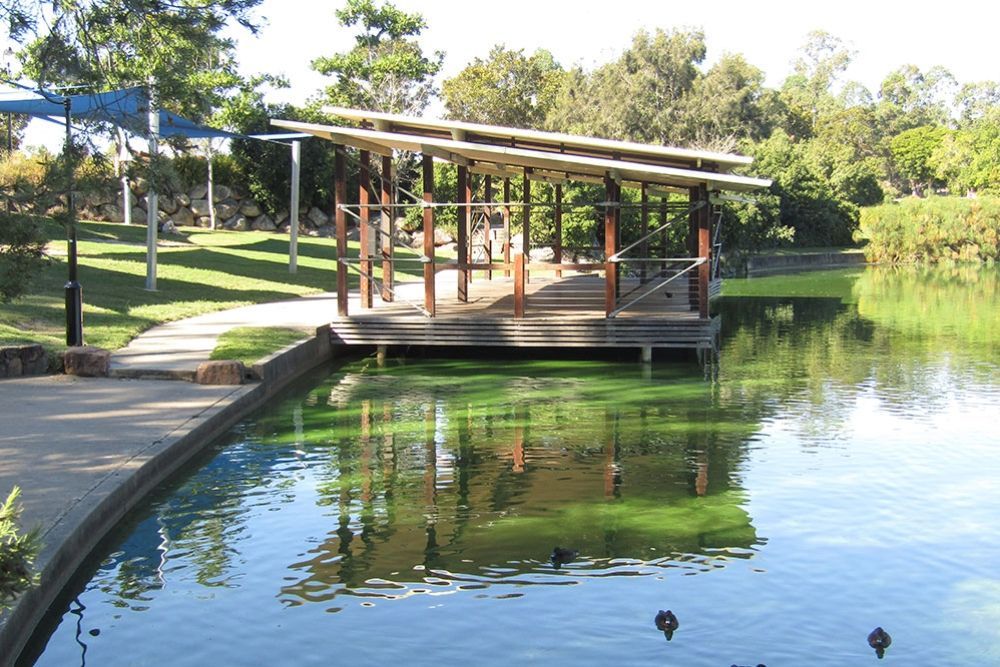 A wooden pavilion extends over a pond, reflecting its structure in Forest Lake.