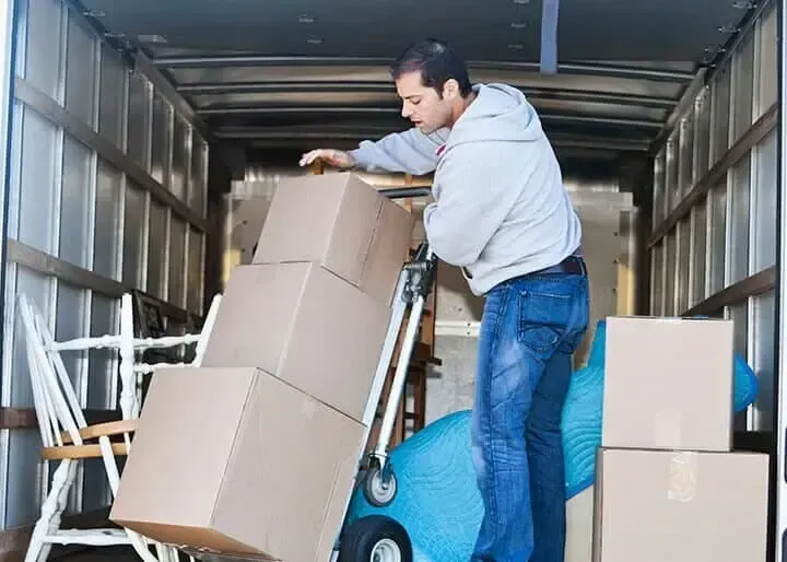 Un hombre carga cajas de cartón en una carretilla manual dentro de un camión de mudanzas.