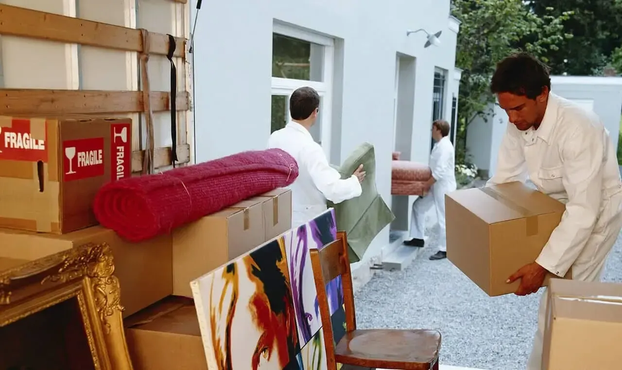 Los transportistas descargan cajas y muebles de un camión a una casa.