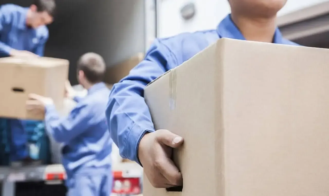 Personal de mudanzas con uniformes azules cargando cajas en un camión.