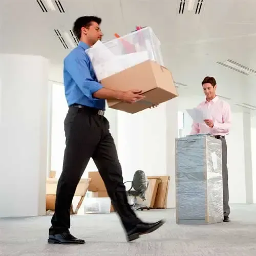Un hombre lleva cajas y un contenedor mientras otro hombre revisa el papeleo en una nueva oficina.