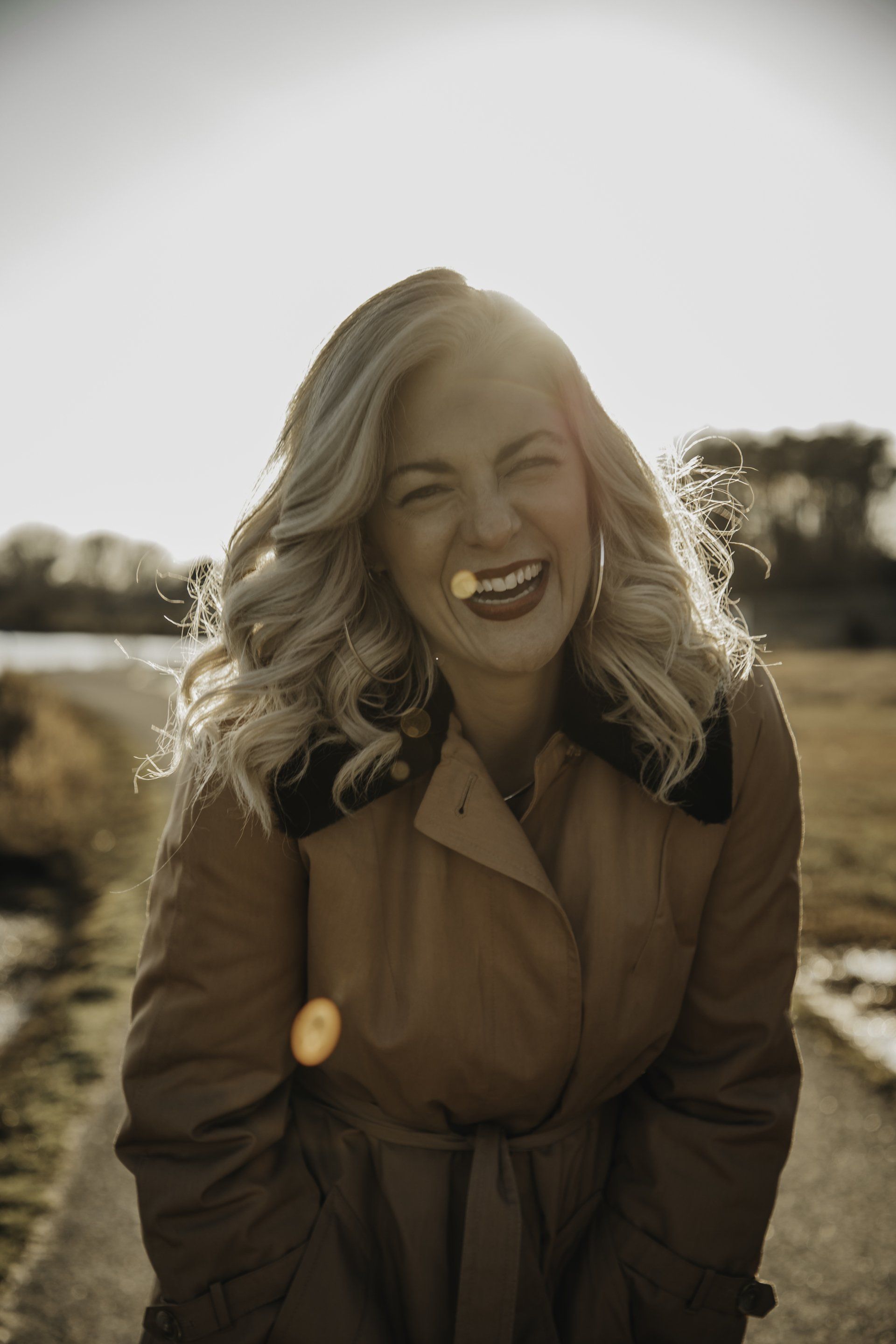 A woman in a trench coat is smiling for the camera.