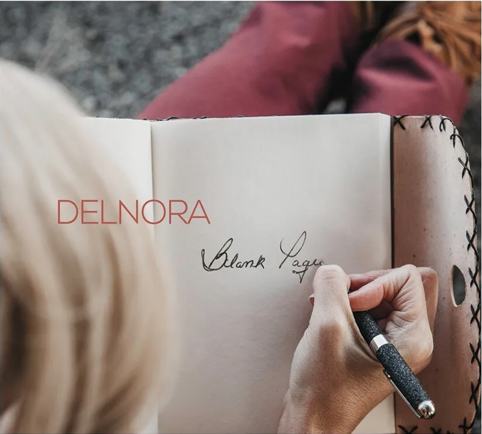 A woman is writing in a notebook with the name delnora on the cover