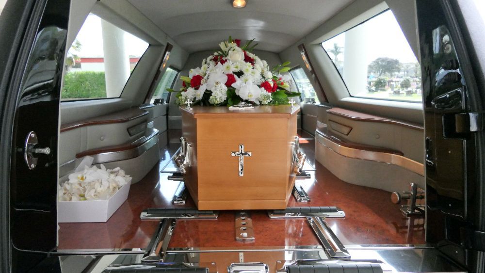 A wooden coffin with a cross on it is in the back of a funeral car.