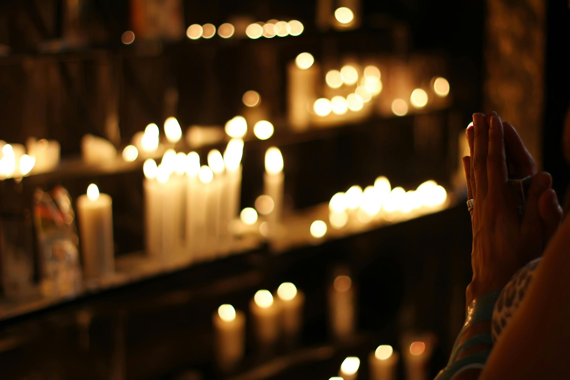 A person is praying in front of a row of lit candles