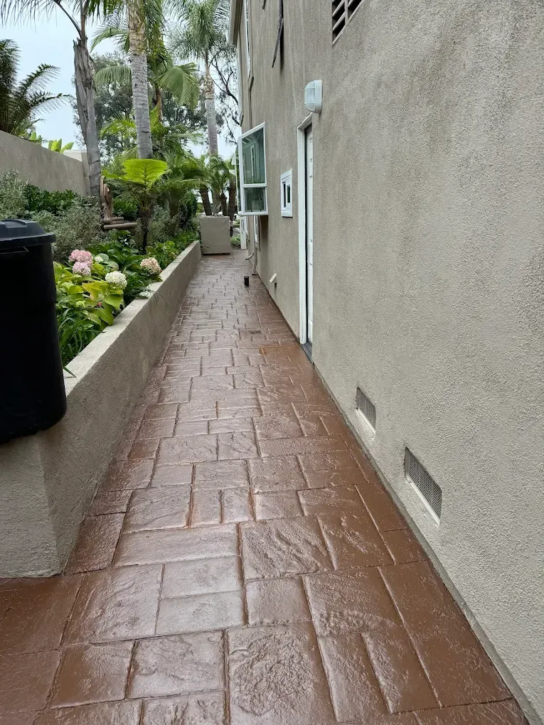 A brick walkway leading to a building with a trash can on the side.