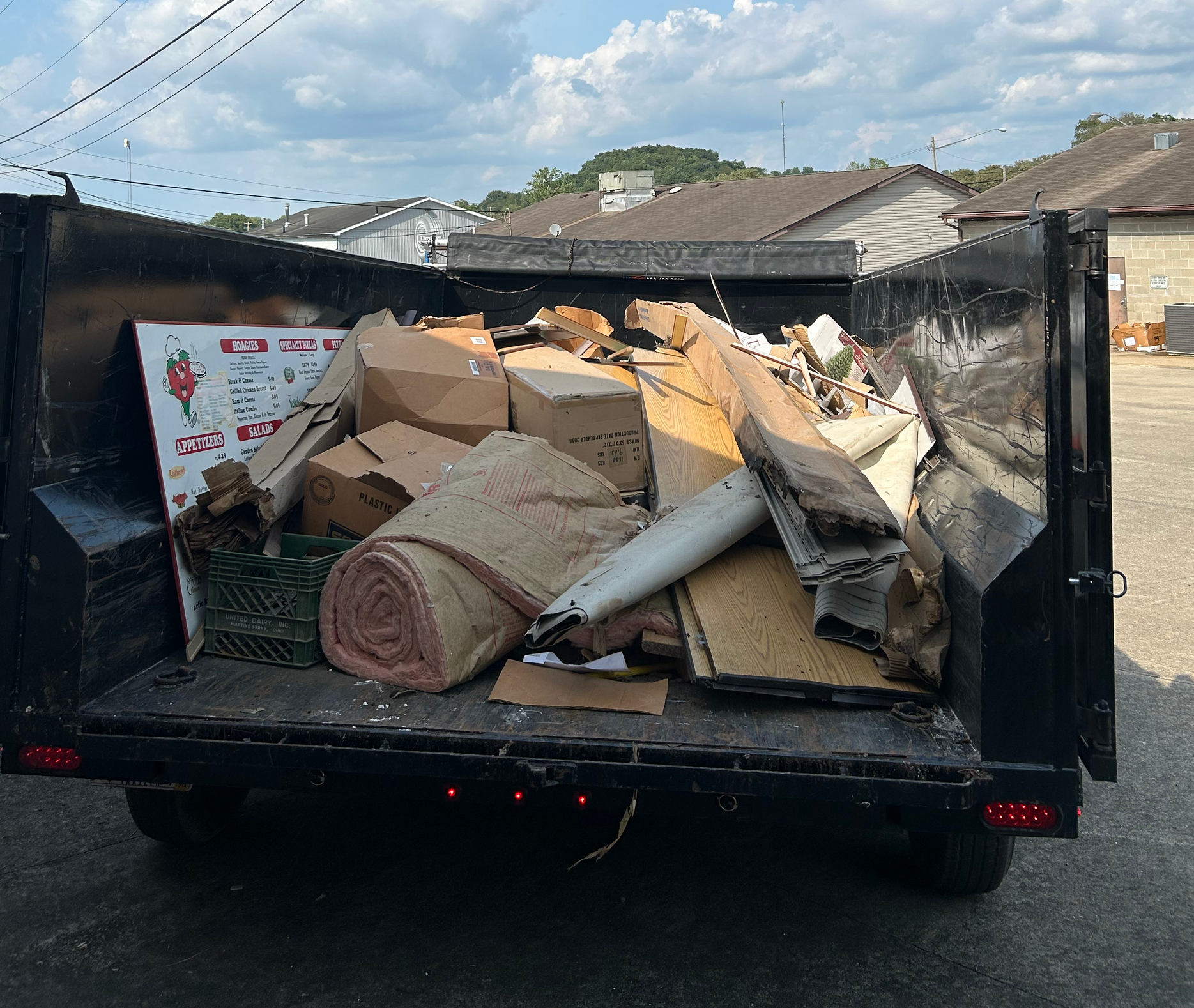 A black trailer filled with construction debris, including cardboard boxes and insulation, outdoors.