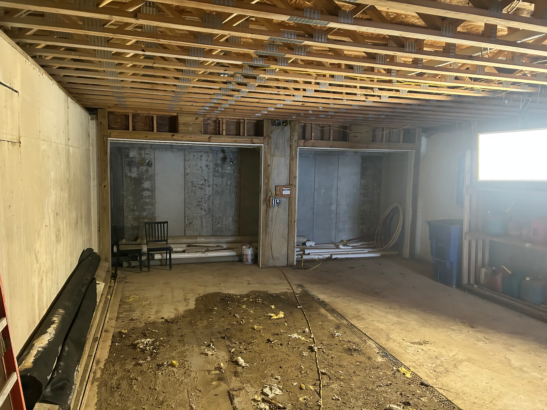 Basement under construction with exposed beams, concrete walls and floor, and two alcoves.
