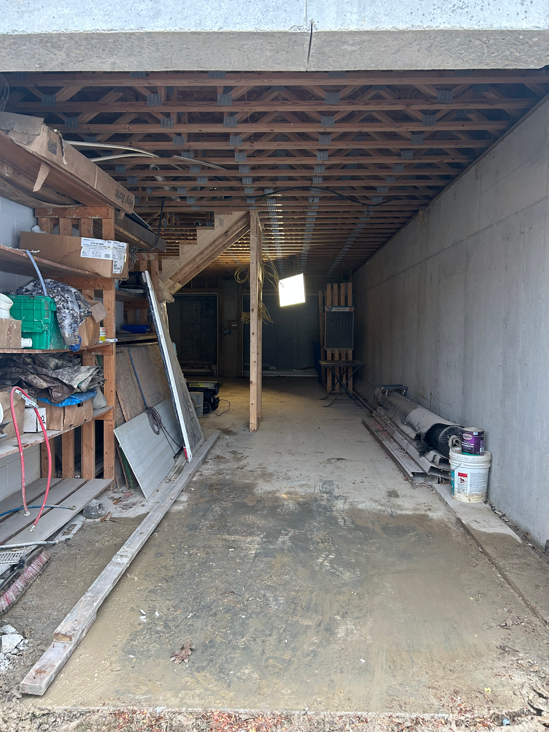 A dark, unfinished basement with concrete walls, exposed ceiling beams, and cluttered shelves.