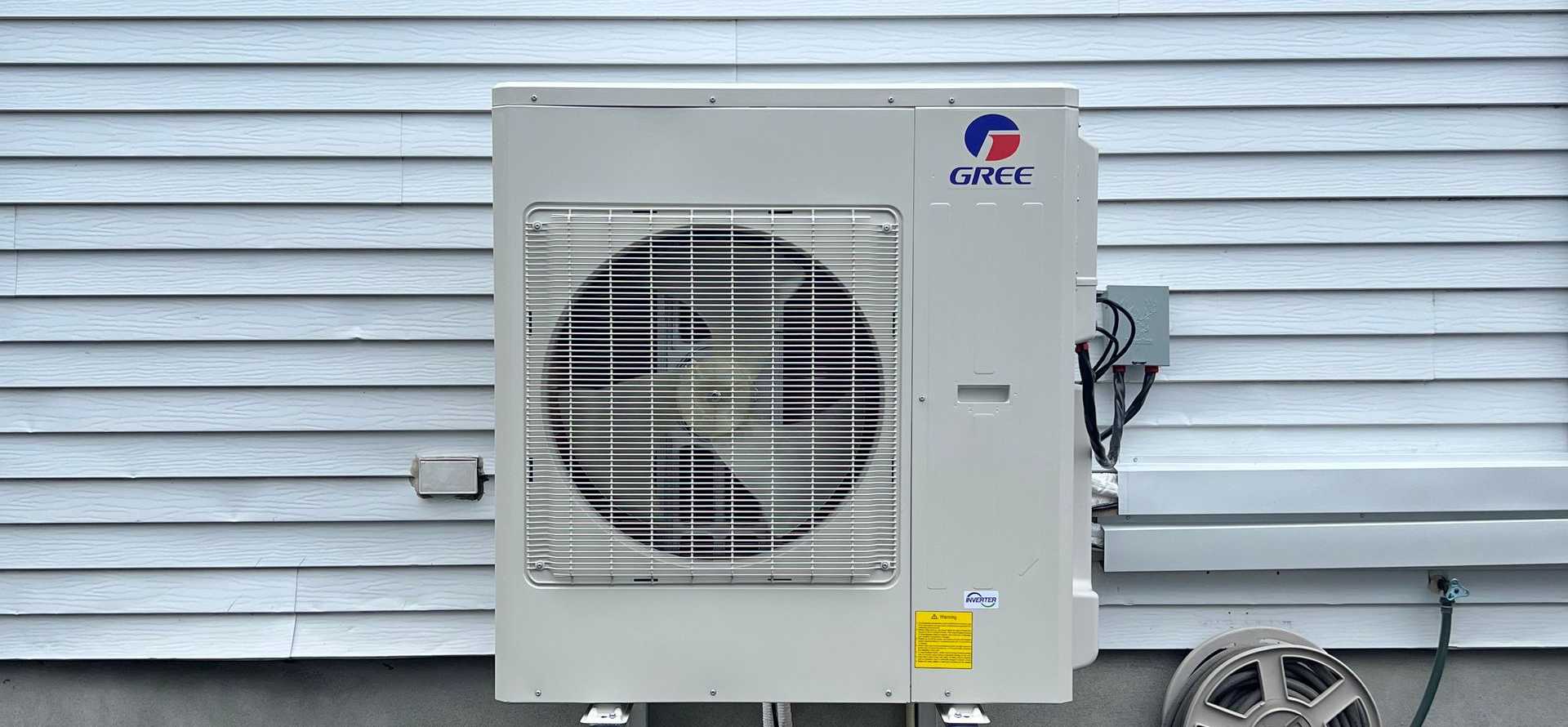 Un climatiseur extérieur beige de marque Gree, monté sur un support métallique sur un toit plat.