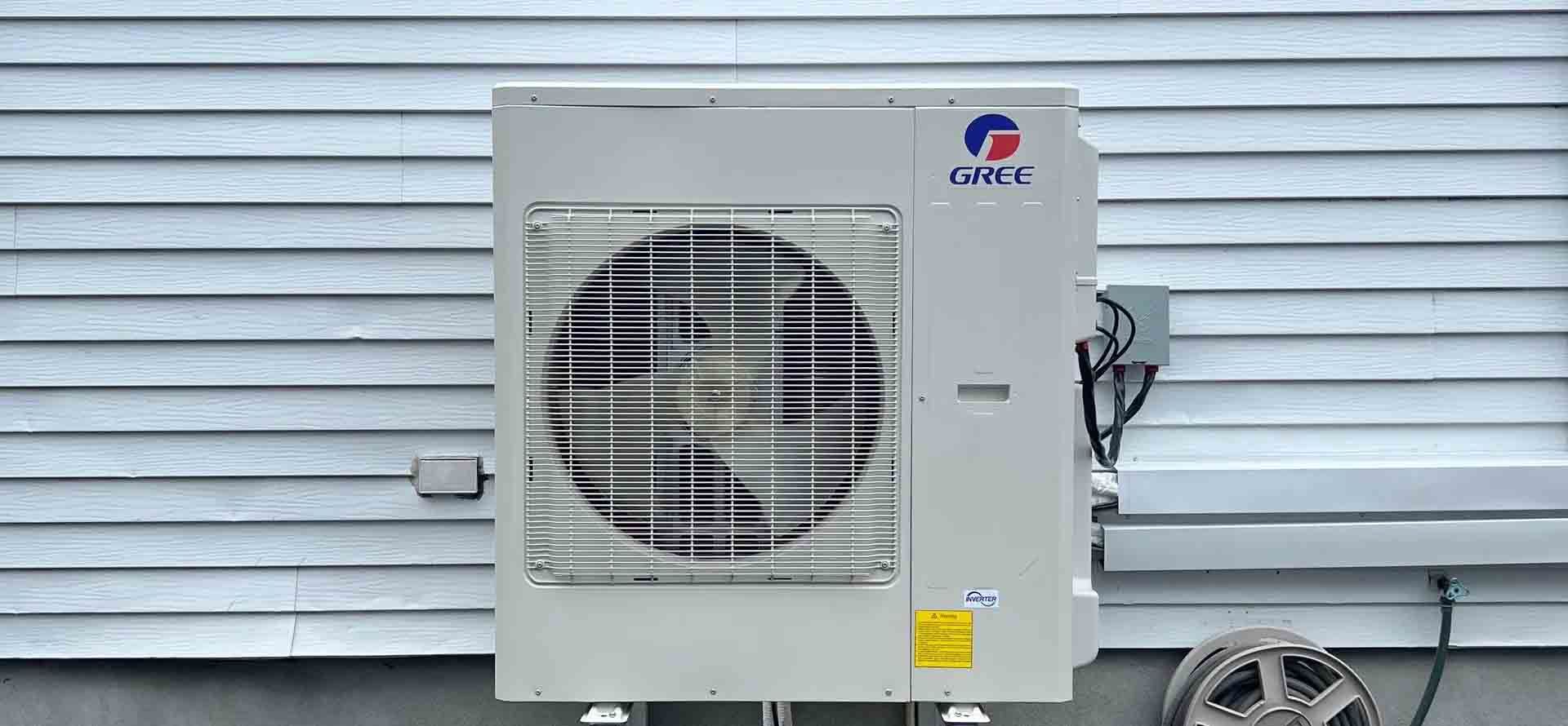 Un climatiseur extérieur beige de marque Gree, monté sur un support métallique sur un toit plat.