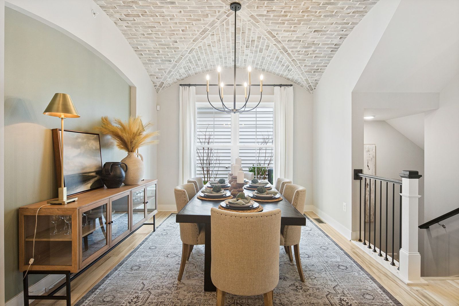 Dining room with brick groin ceiling, chandelier, long table with place settings, sideboard, rug.