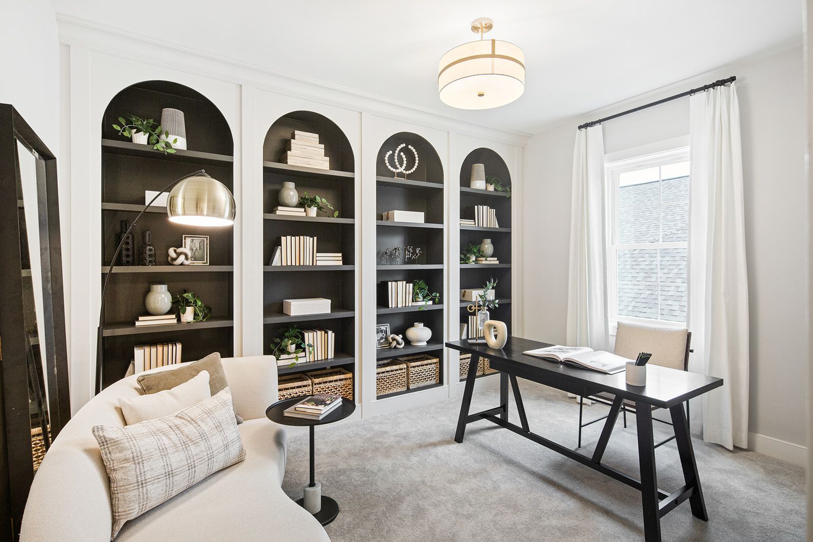 Home office with built-in arched bookshelves, black desk, light-colored sofa, and a large mirror.