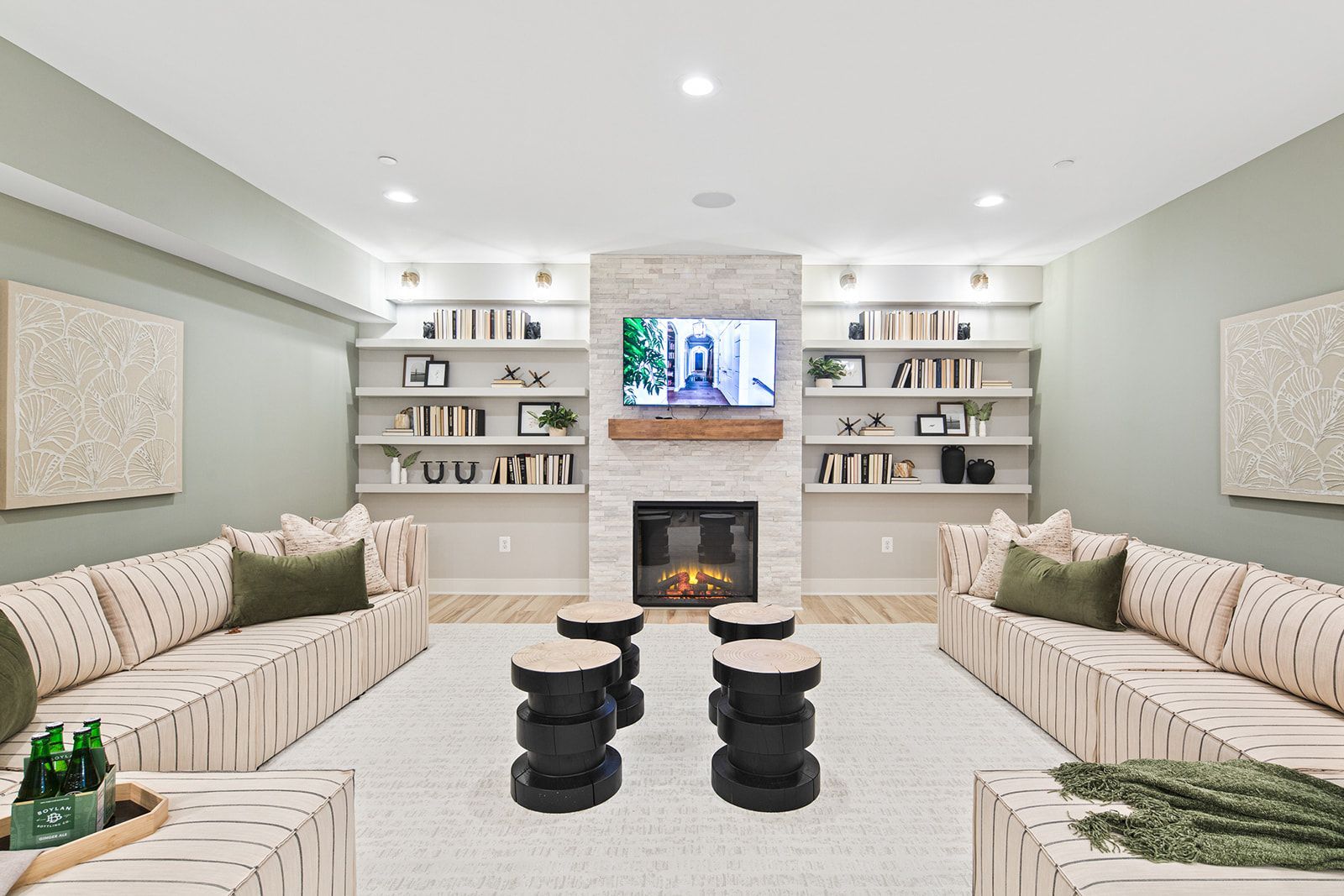 Cozy living room with sofas, fireplace, TV, bookshelves, and dark stools on a rug.