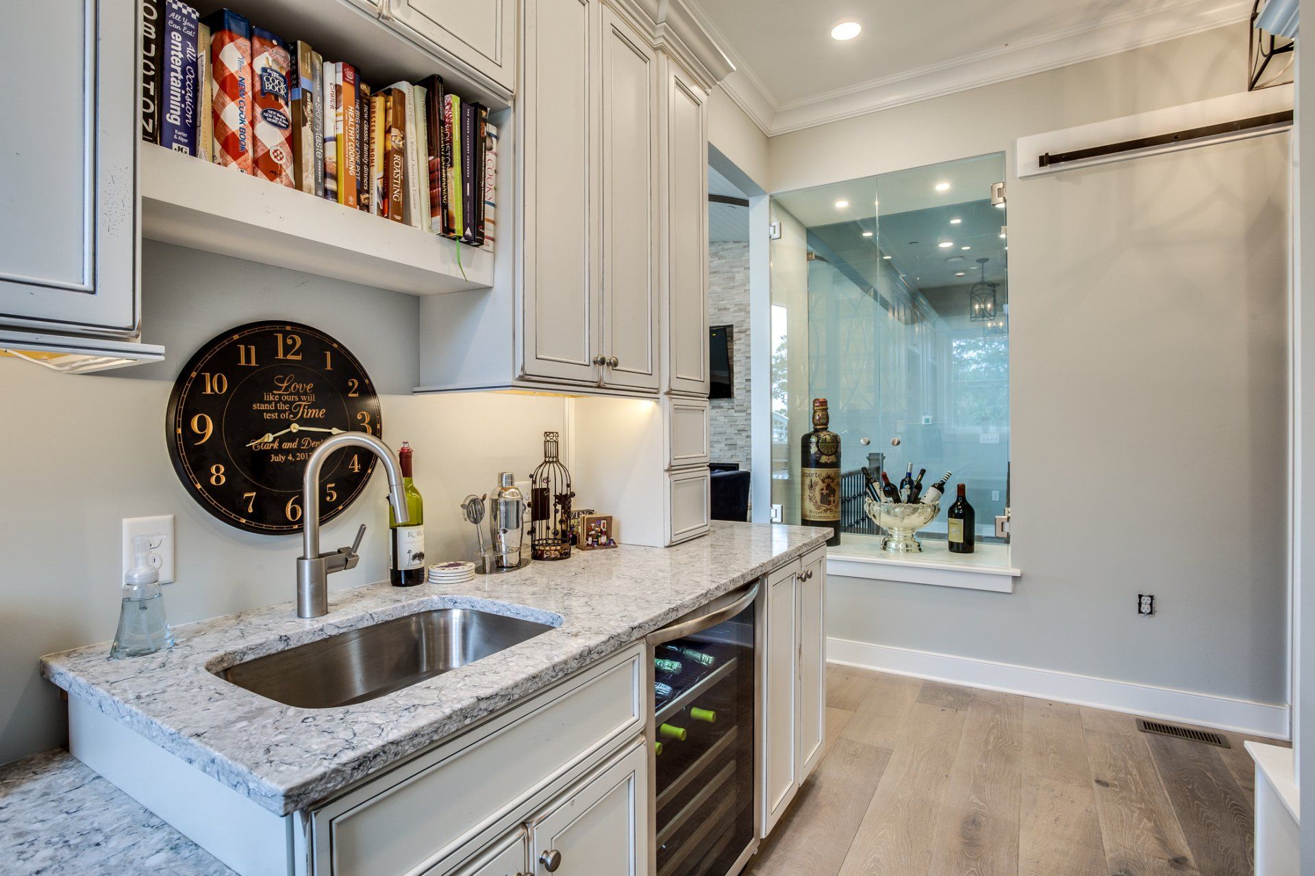 A small, white-cabinet bar with a granite countertop, sink, wine cooler, and glass-walled wine storage.