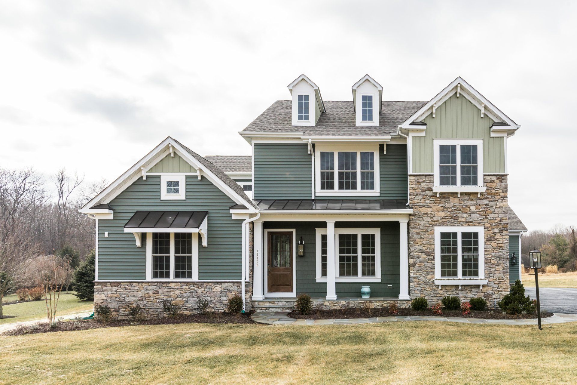 Two-story house with green siding, stone accents, and a brown door under a cloudy sky.