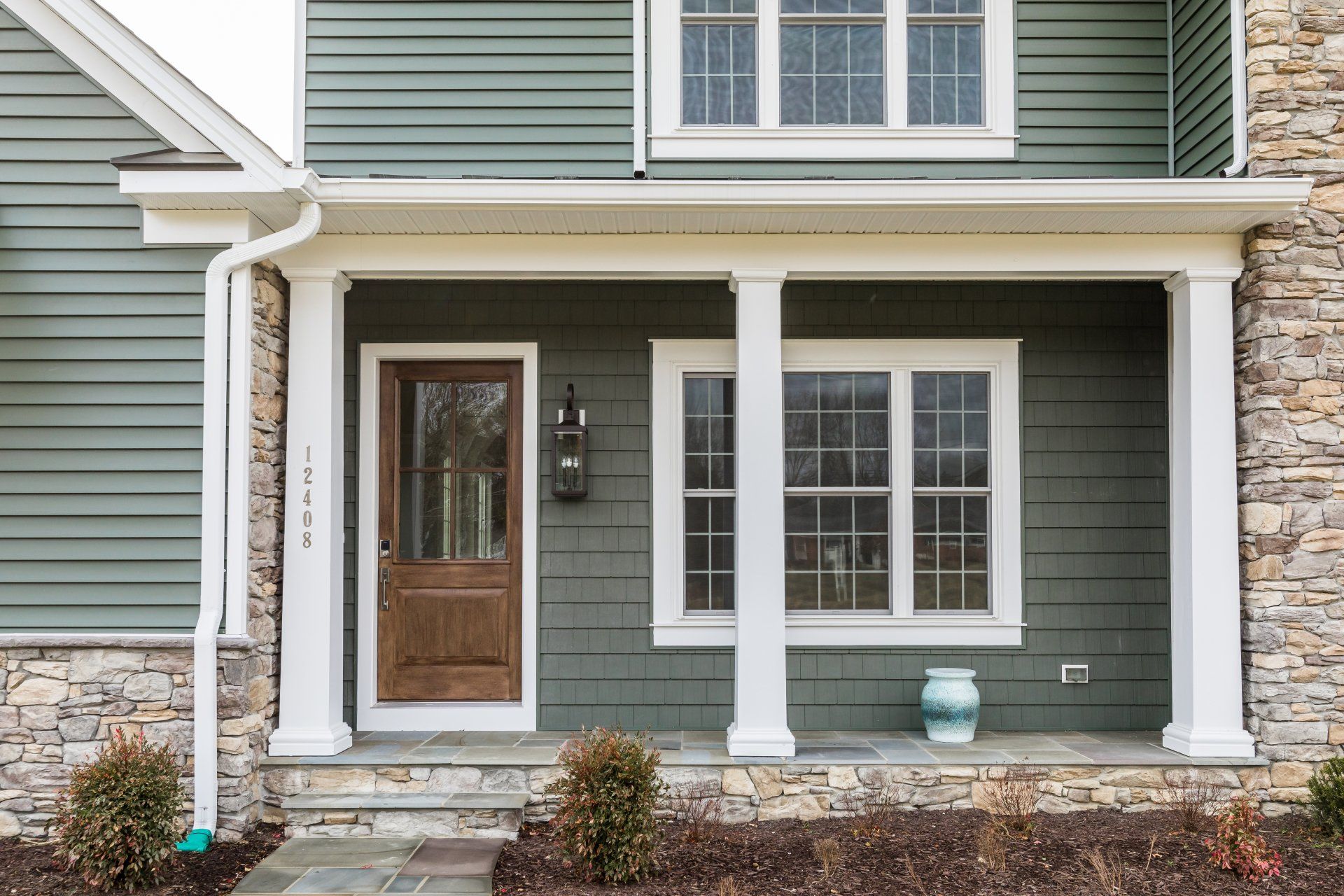 Green house exterior with a brown door, white columns, stone accents, and a front porch.