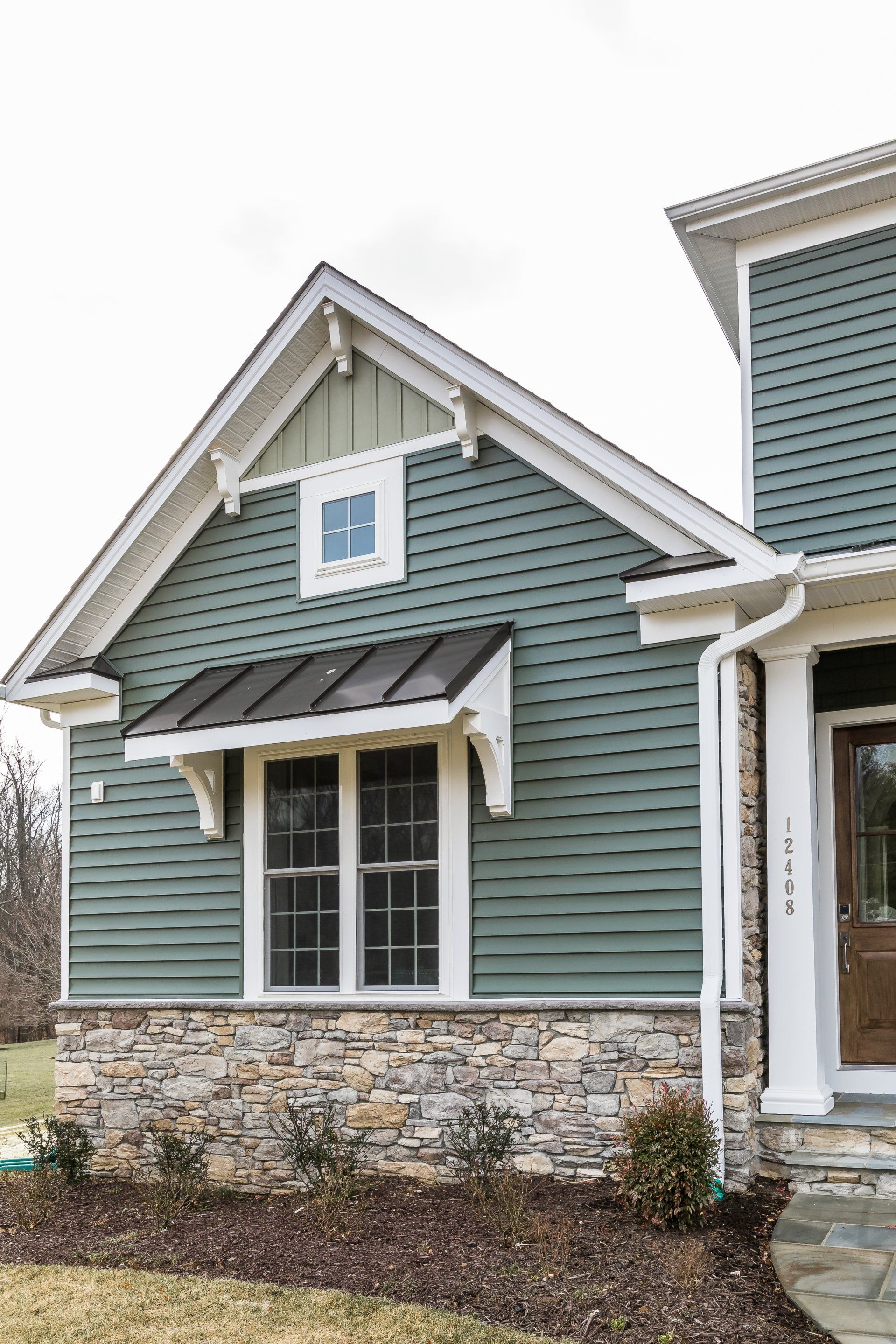 Green siding house with stone base, a window with a black awning.