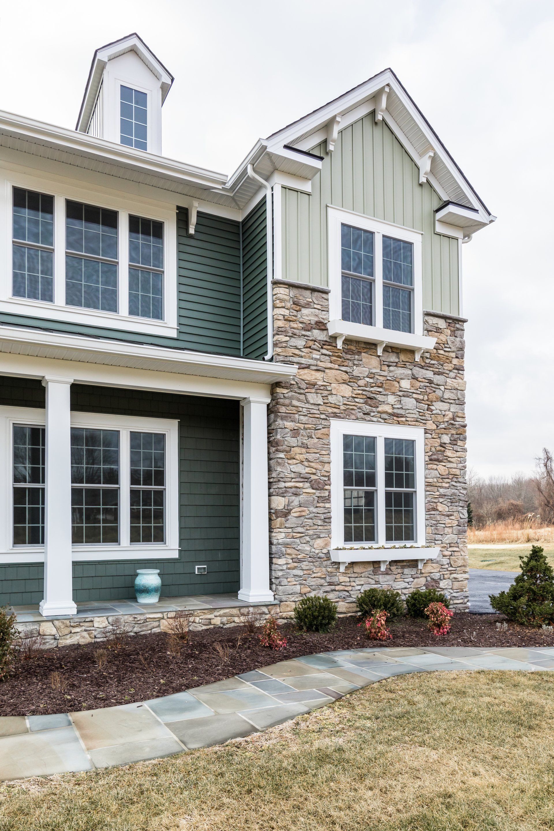 Two-story house with green siding, stone facade, white trim, and a blue front door.