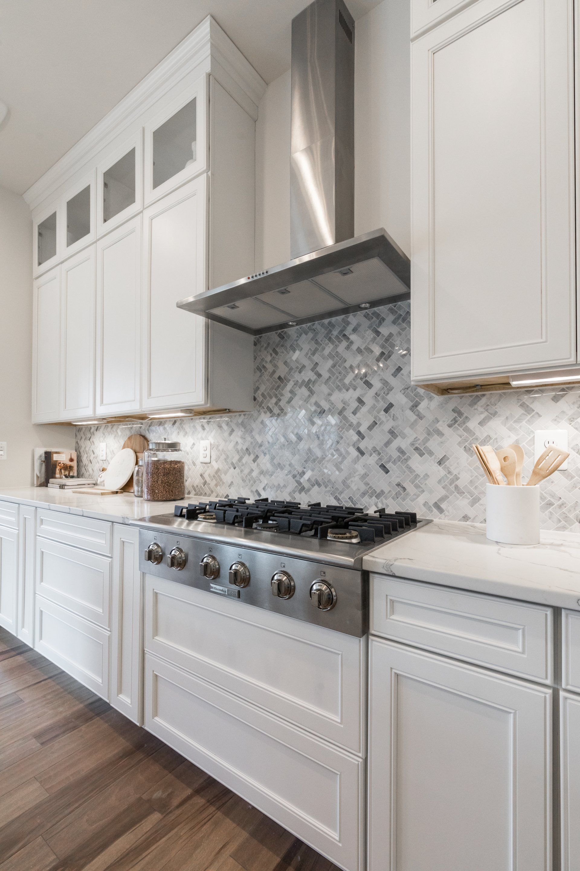 White kitchen with stainless steel appliances, marble backsplash, and light wood floors.
