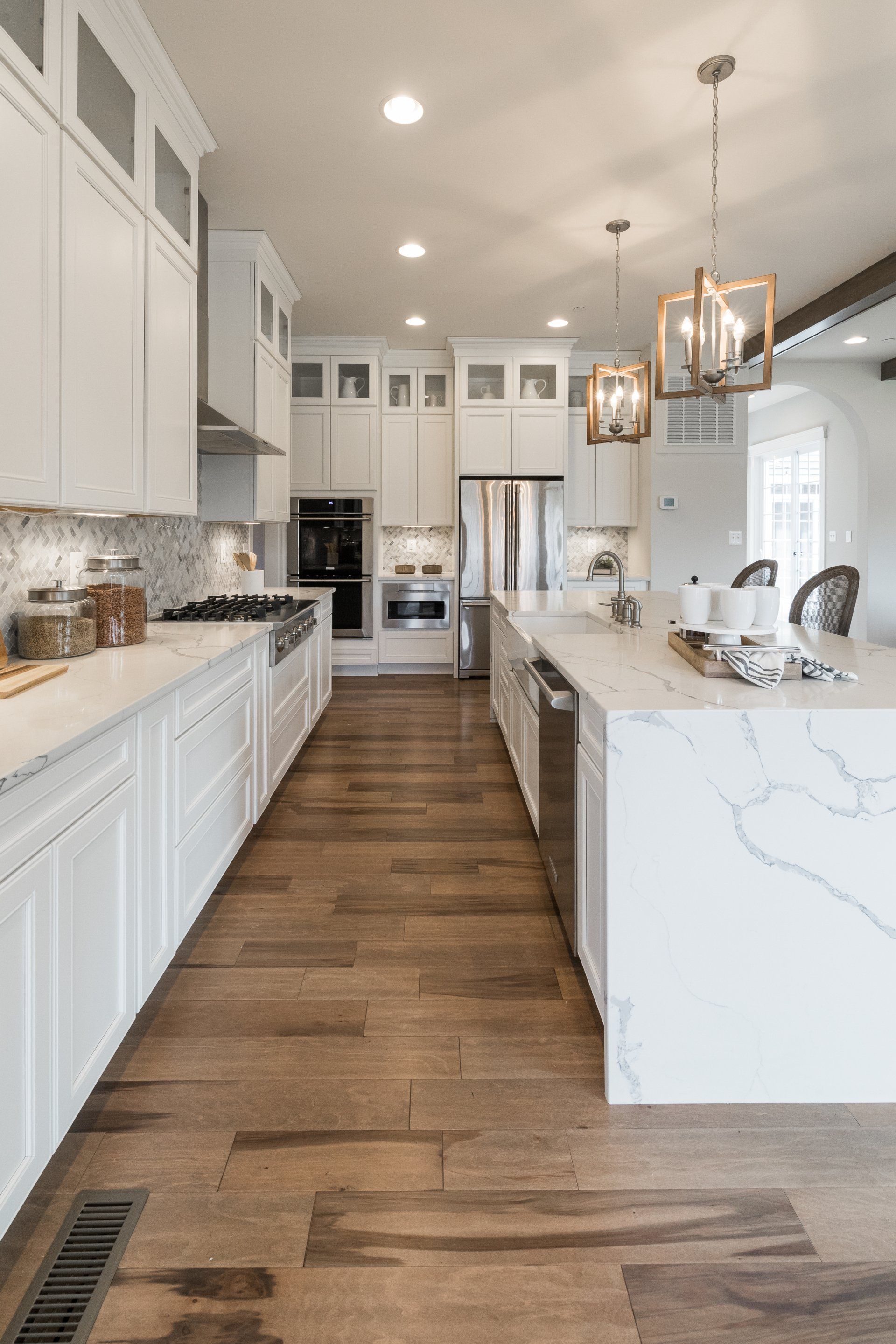 Spacious, modern white kitchen with wooden floors, a large island, and pendant lights.