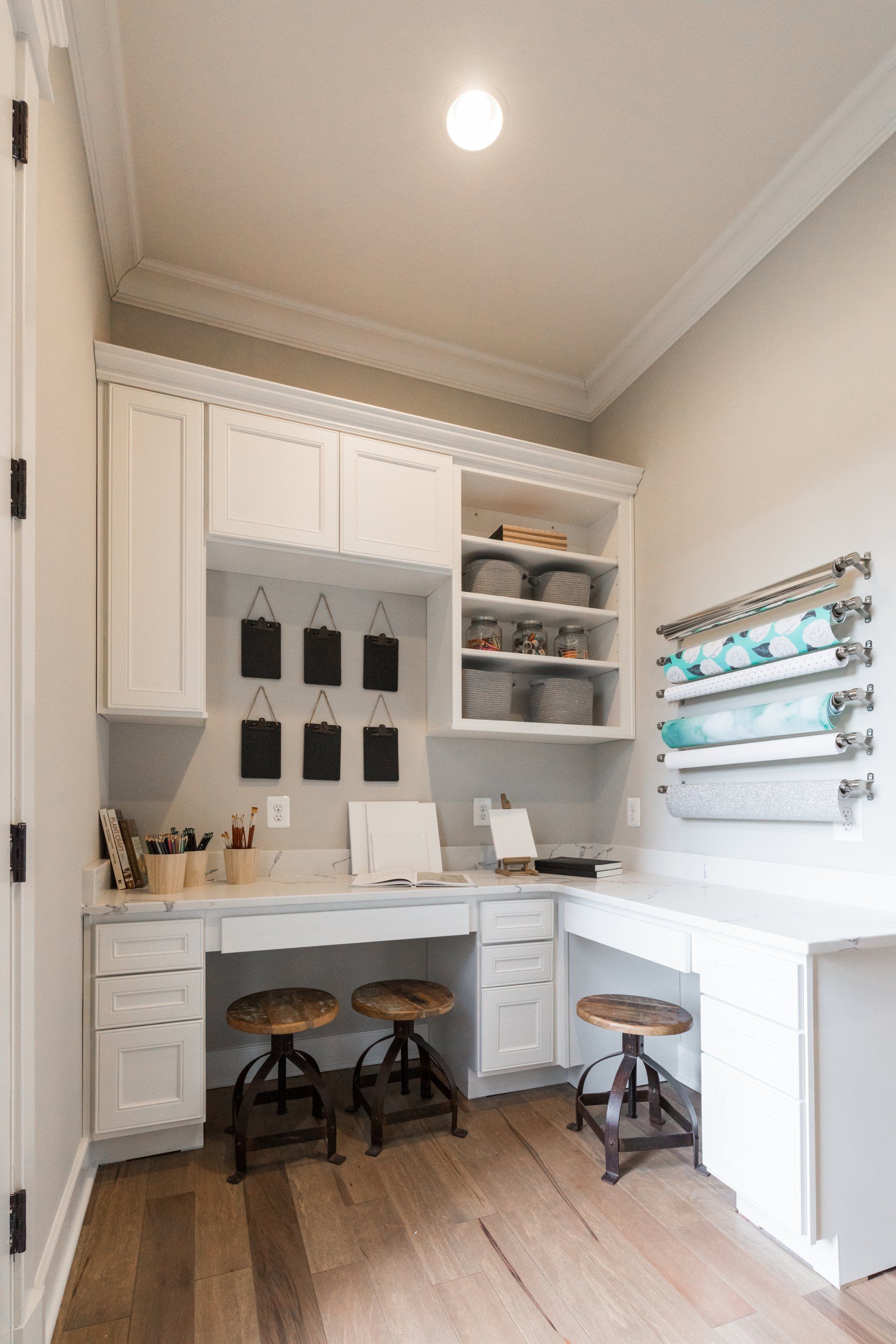 Craft room with white cabinets, two desks, and wooden floor.  Black chalkboards, storage baskets, and stools.