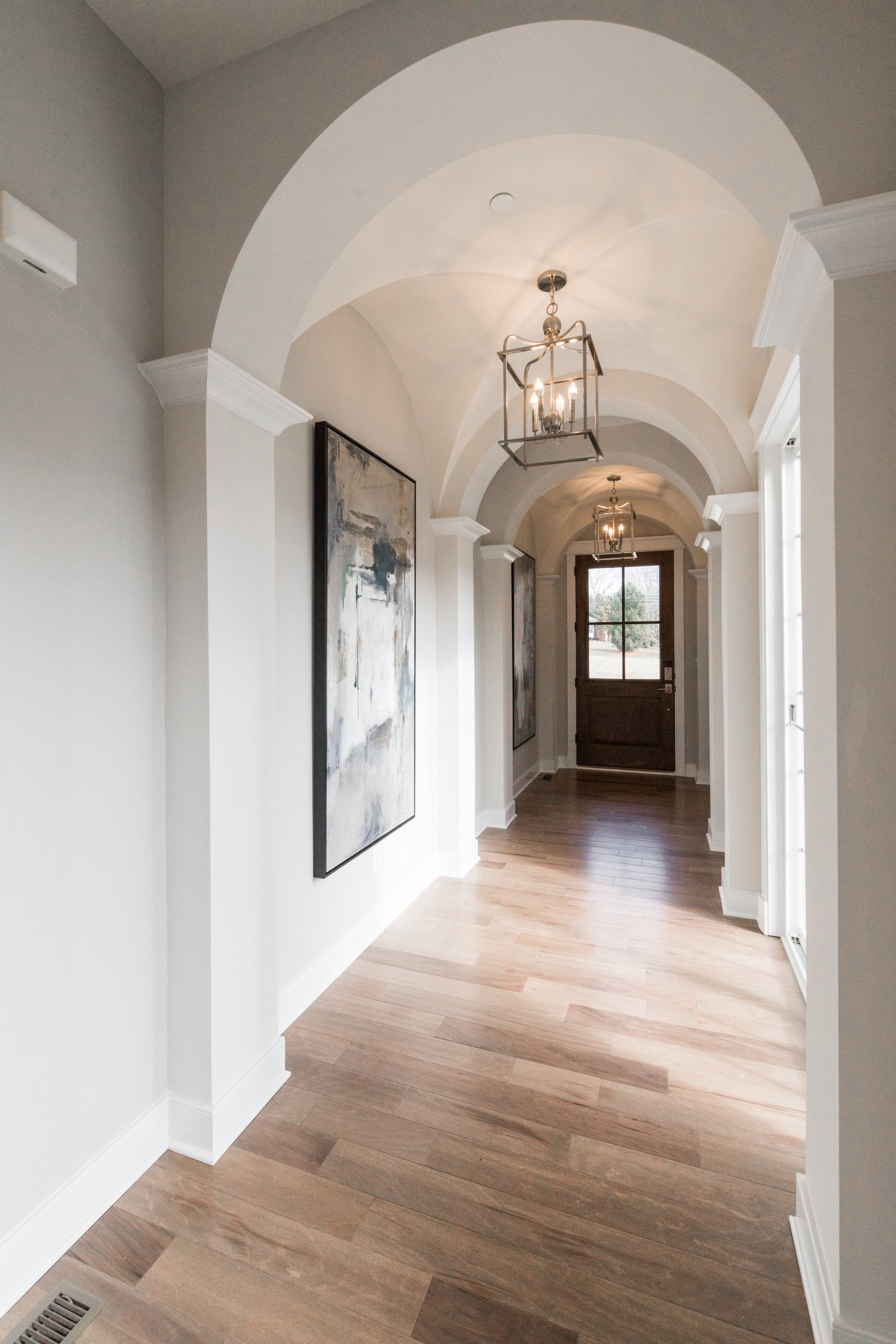 Hallway with arched ceiling, wood floors, artwork, and a front door.