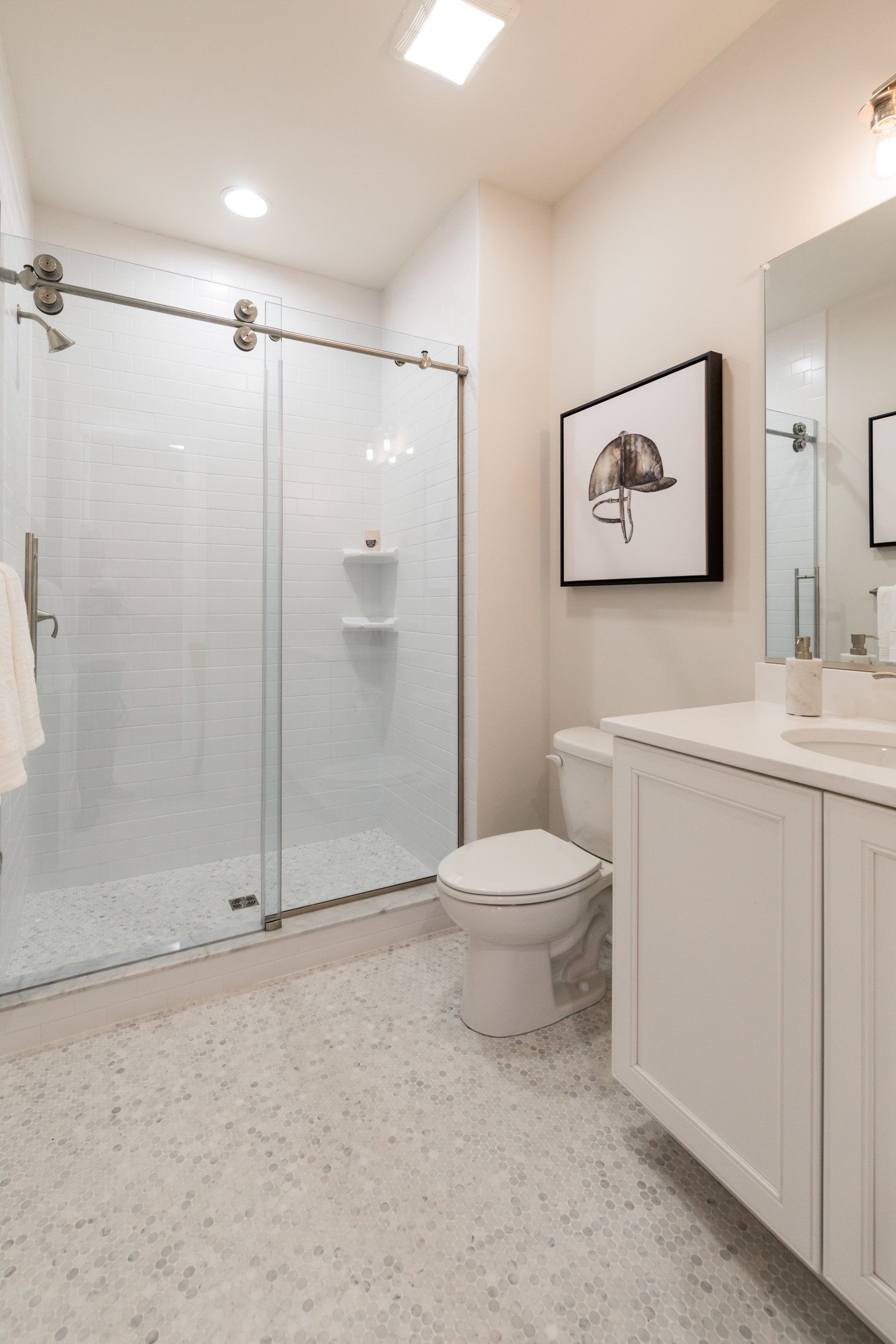 Bathroom with glass shower, white vanity, toilet, and a black-framed artwork. White and light grey tones.