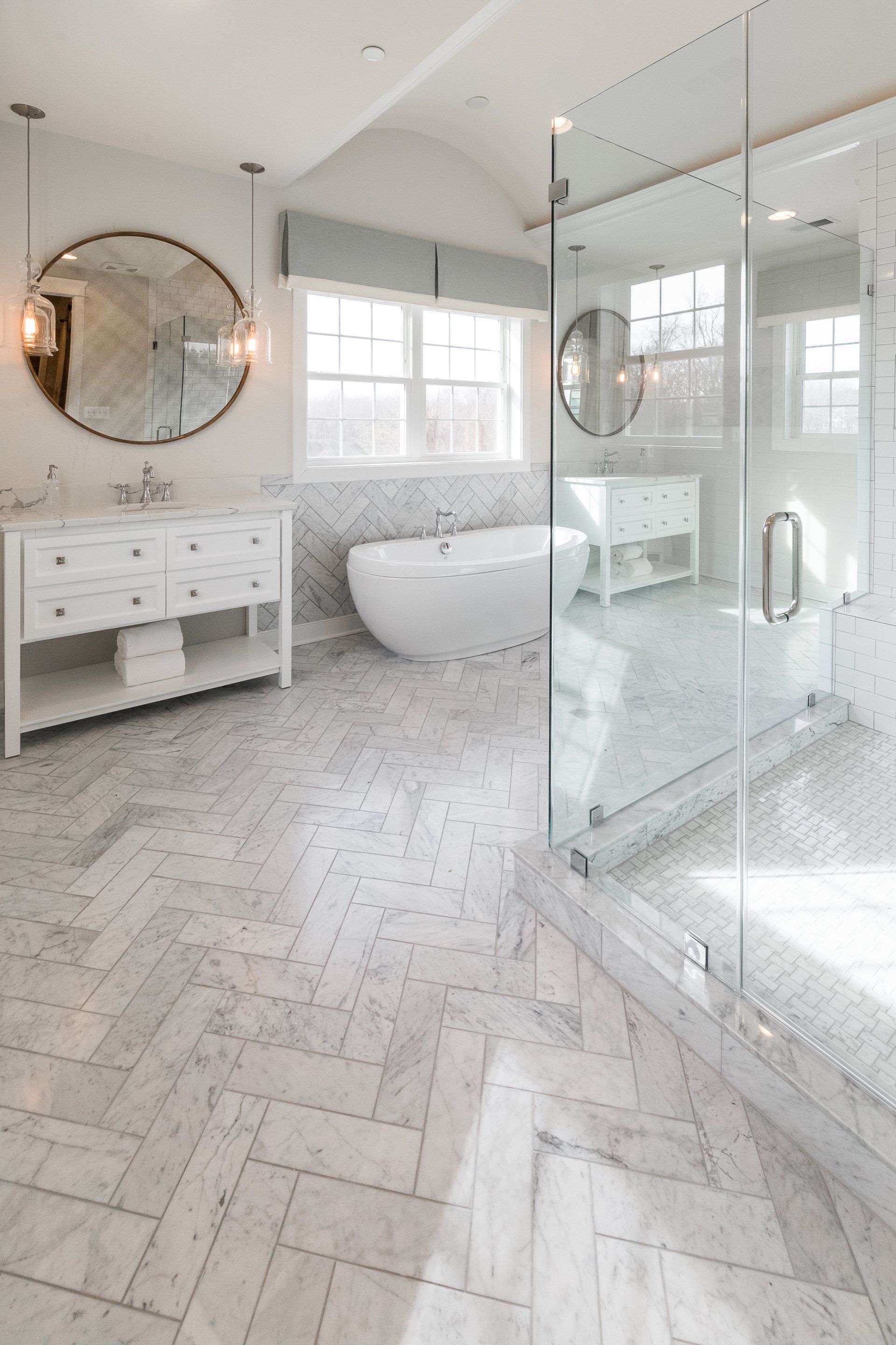 Elegant white bathroom with marble herringbone floors, a freestanding tub, and a glass shower.