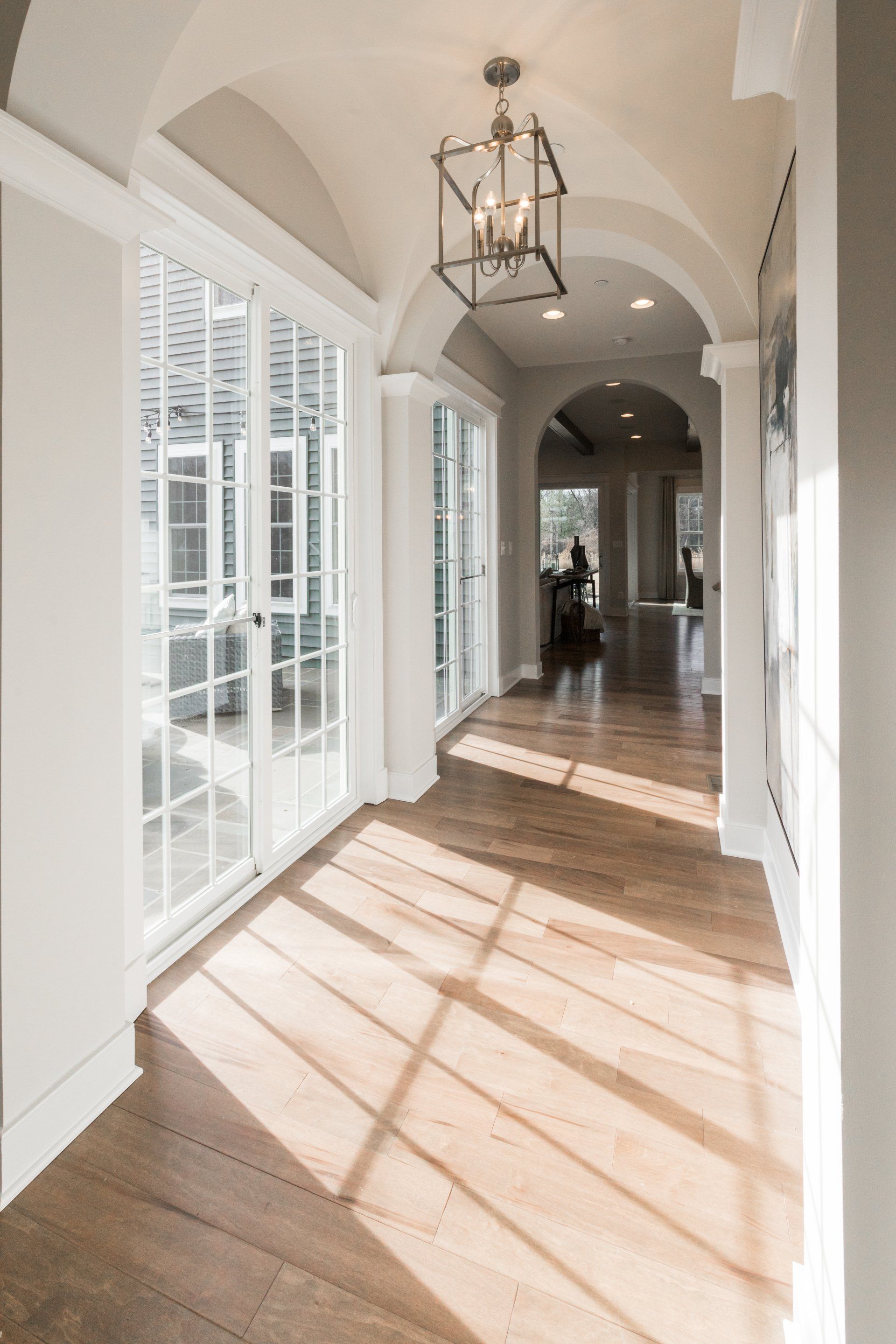 Hallway with arched ceiling, glass doors, hardwood floors, and a hanging light.