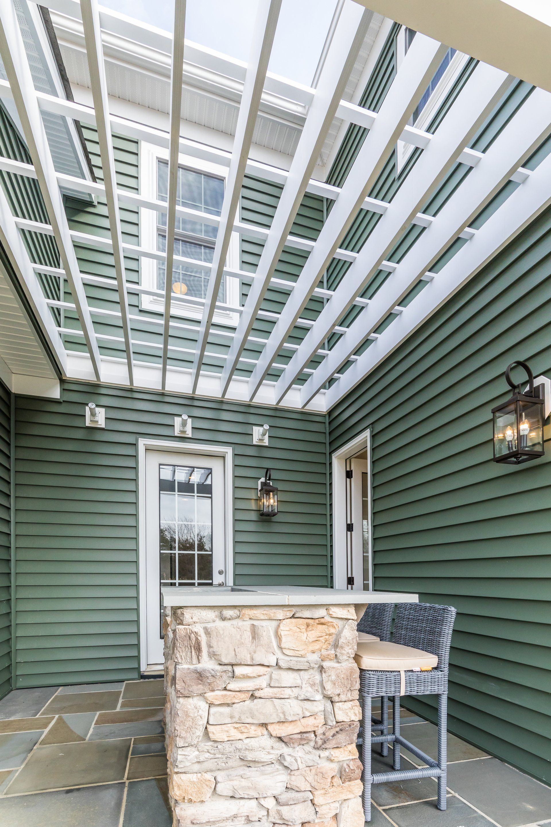 Covered outdoor patio with stone bar, green siding, and a pergola.