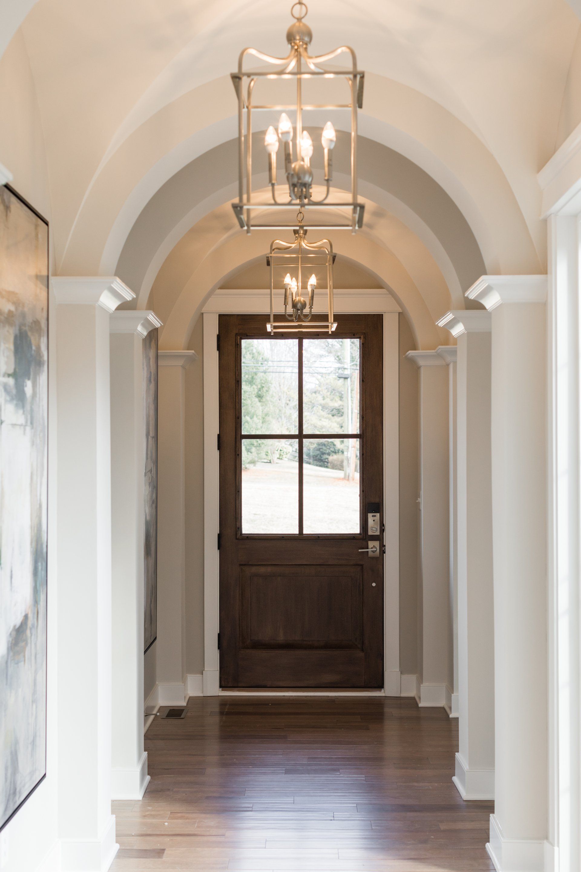 Arched hallway with a dark wood door, two pendant lights, and hardwood floors.