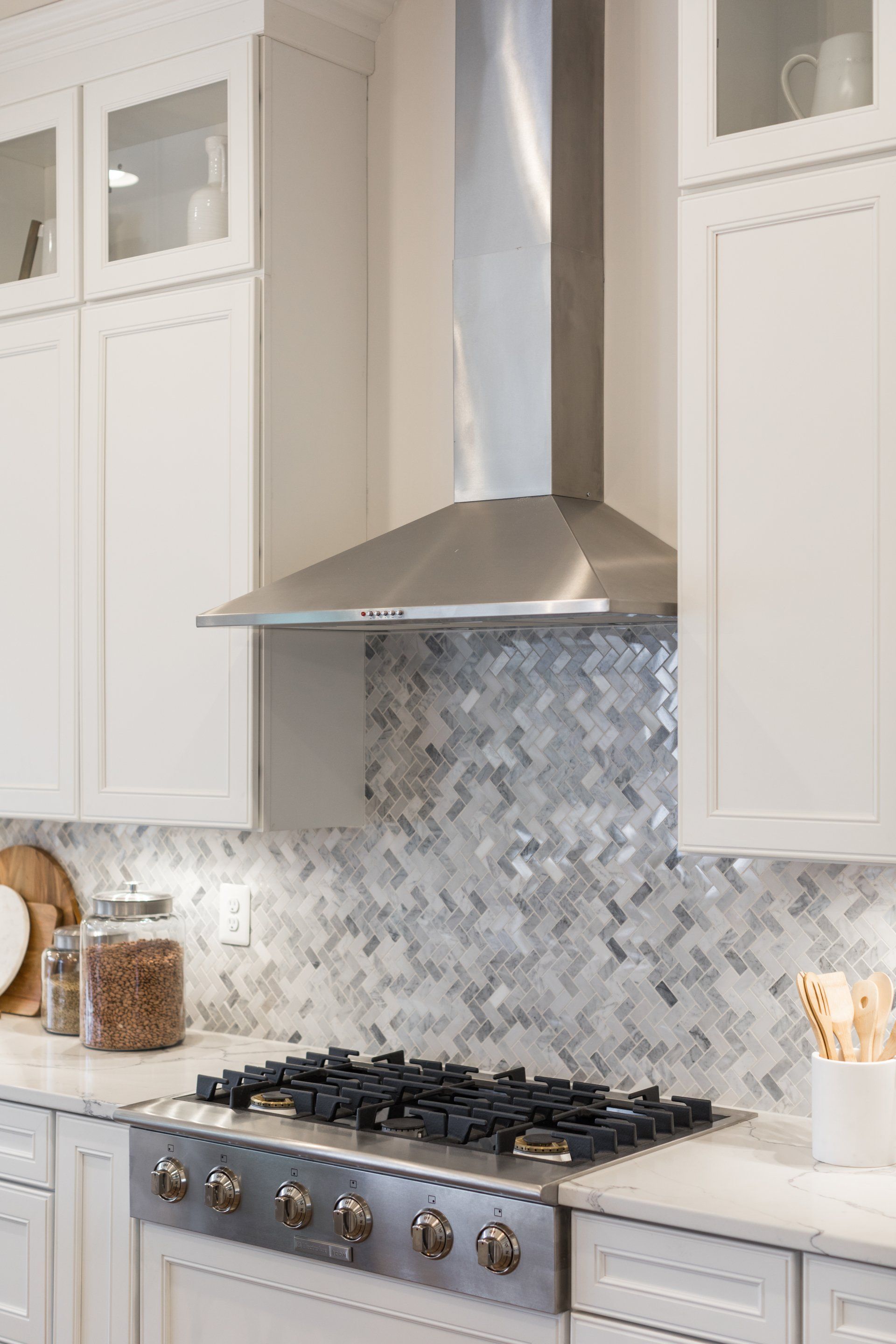 White kitchen with a stainless steel range hood over a gas stovetop and white cabinets.