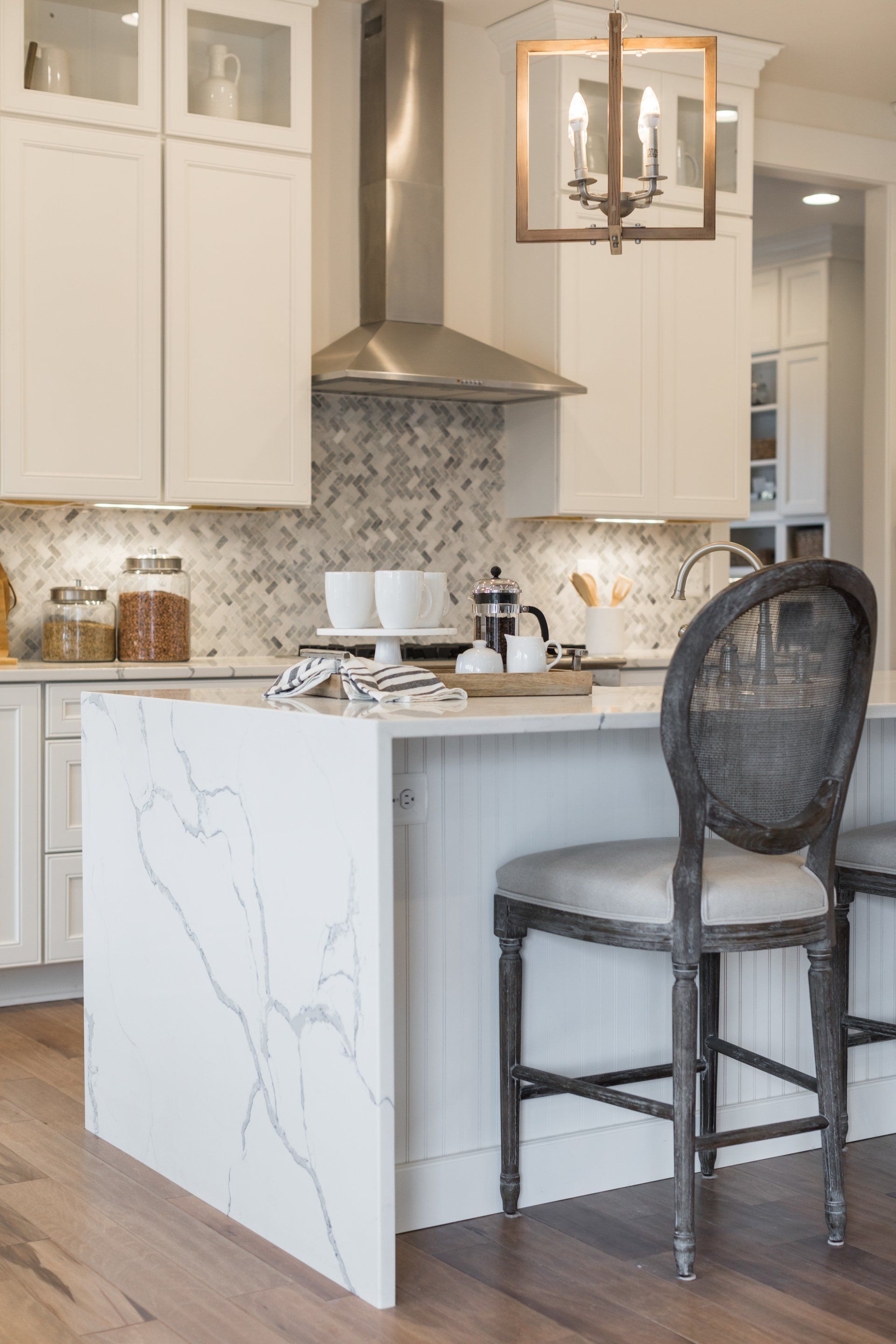 White kitchen with marble island, range hood, and cane-backed bar stool.