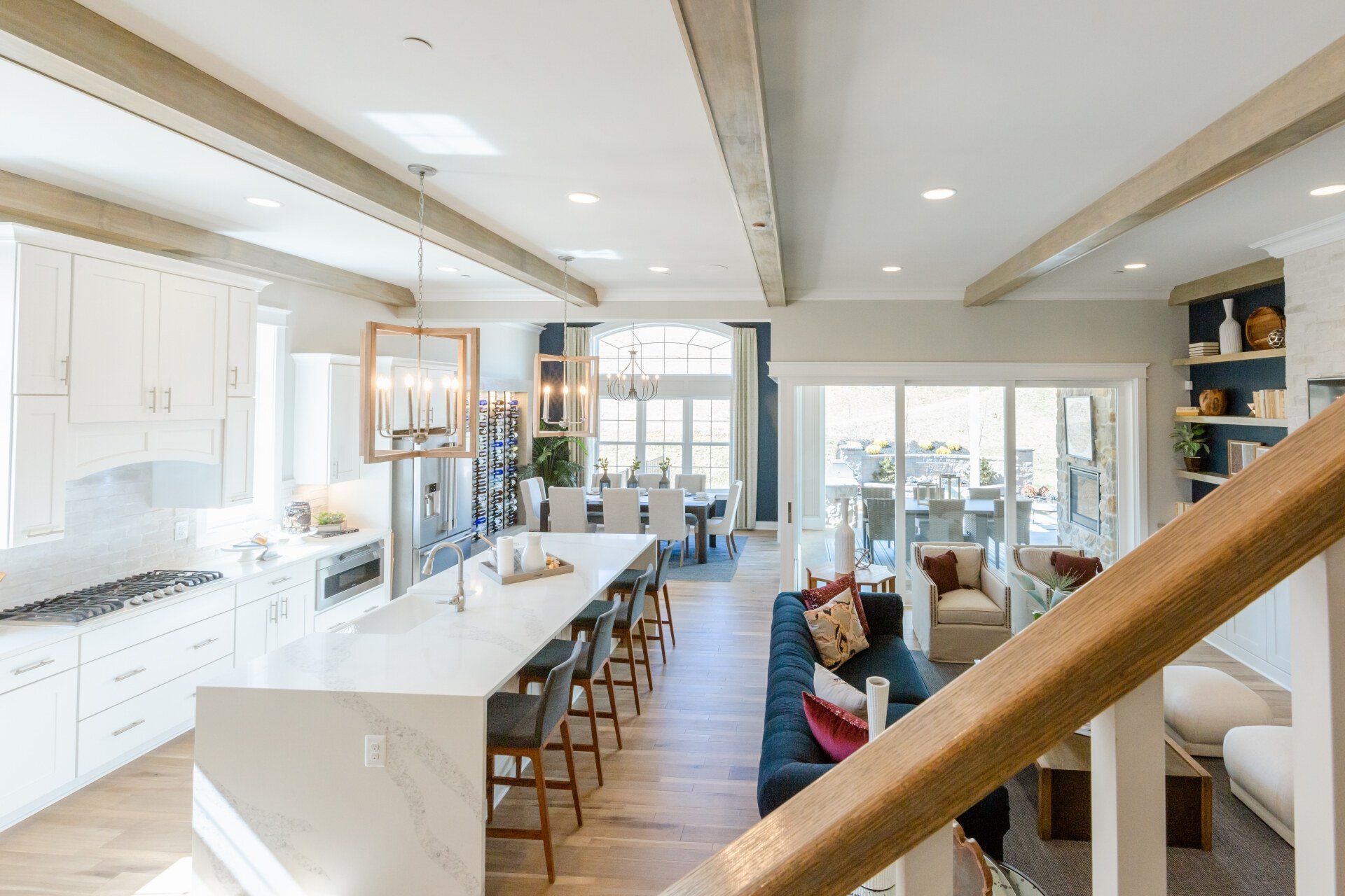 Open-concept kitchen and living area with a large island, white cabinetry, and wooden beams.