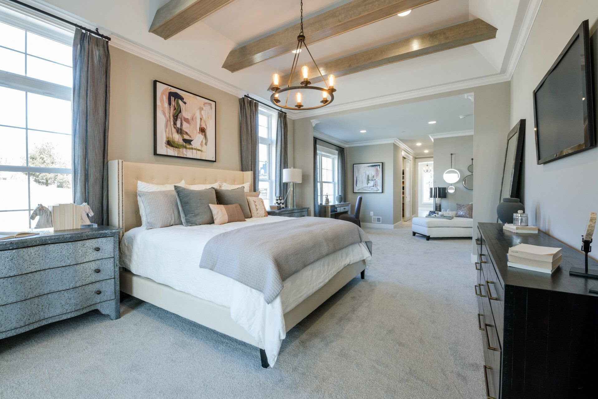 Bedroom with a bed, dressers, artwork, and a chandelier; neutral colors and modern design.