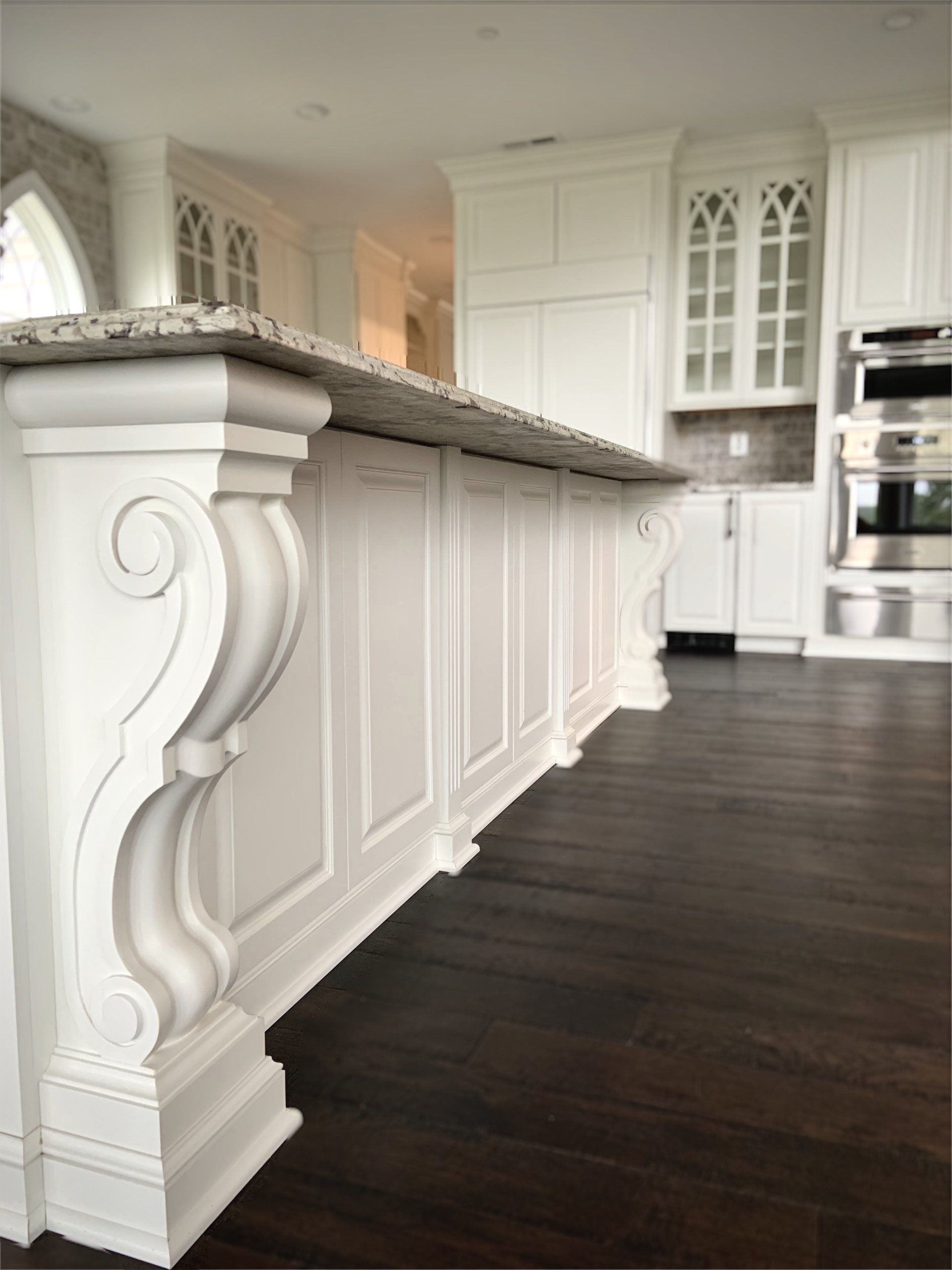White kitchen island with ornate corbels and granite countertop. Dark wood floor.
