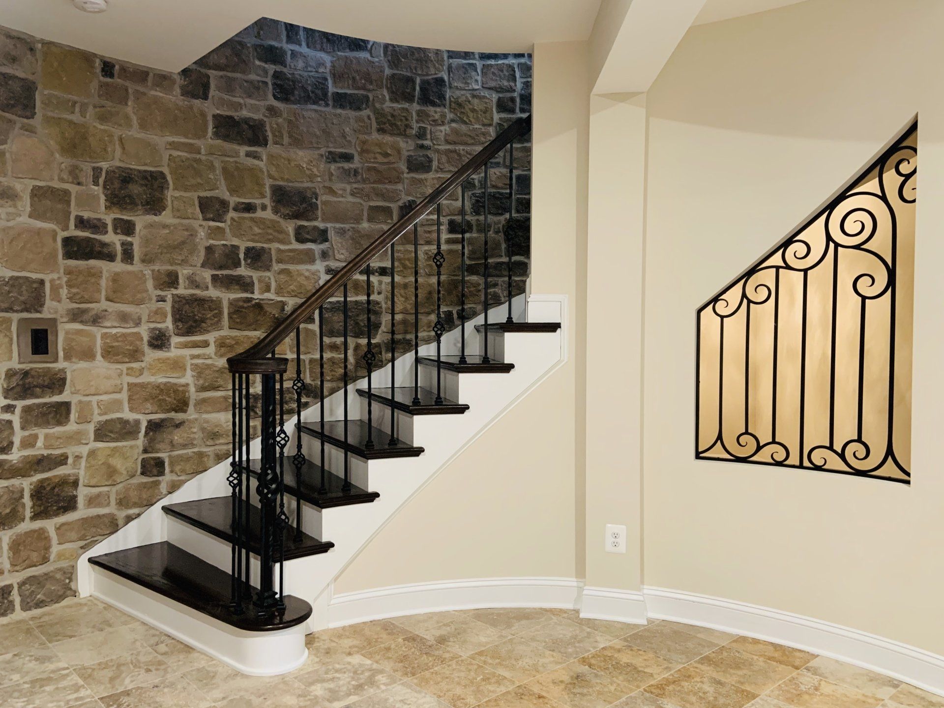 Staircase with black treads, metal railing, stone wall, and decorative ironwork on a beige wall.