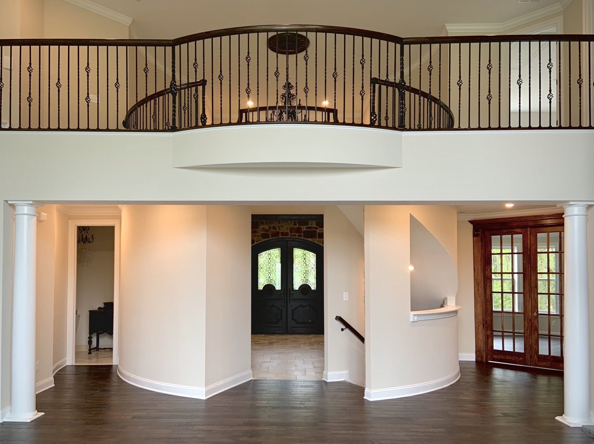 Open foyer with a dark wooden floor, curved walls, and a second-floor balcony with wrought-iron railing.