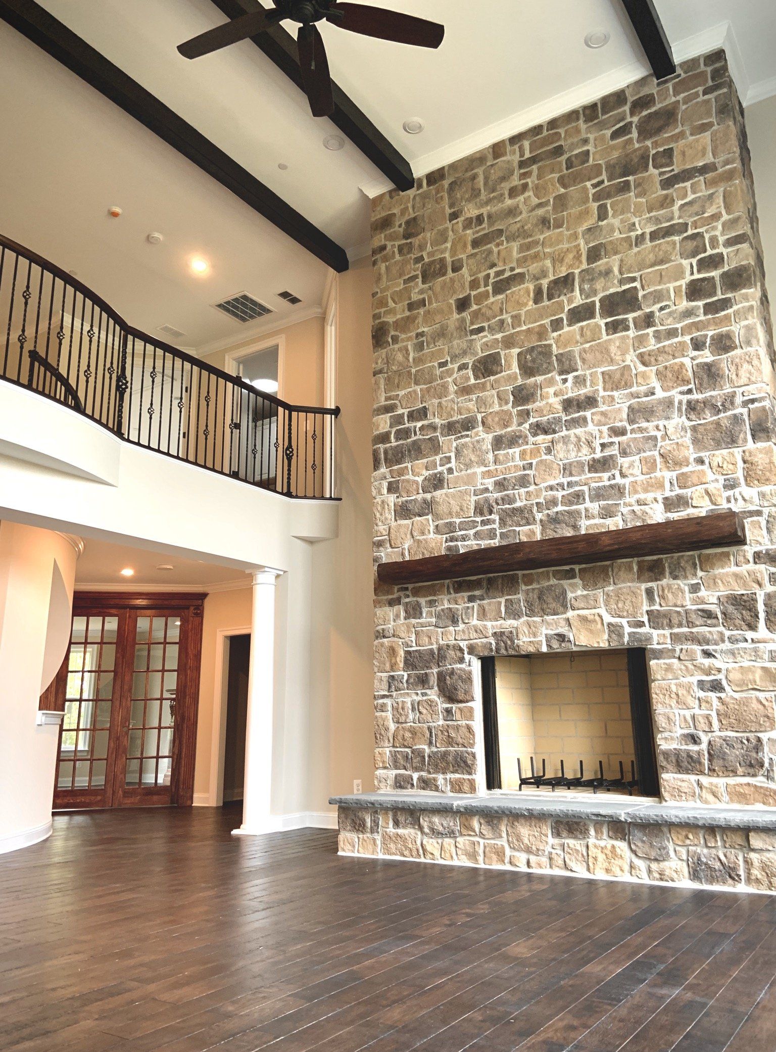 Stone fireplace in a large room with dark wood floors and a second-story balcony.
