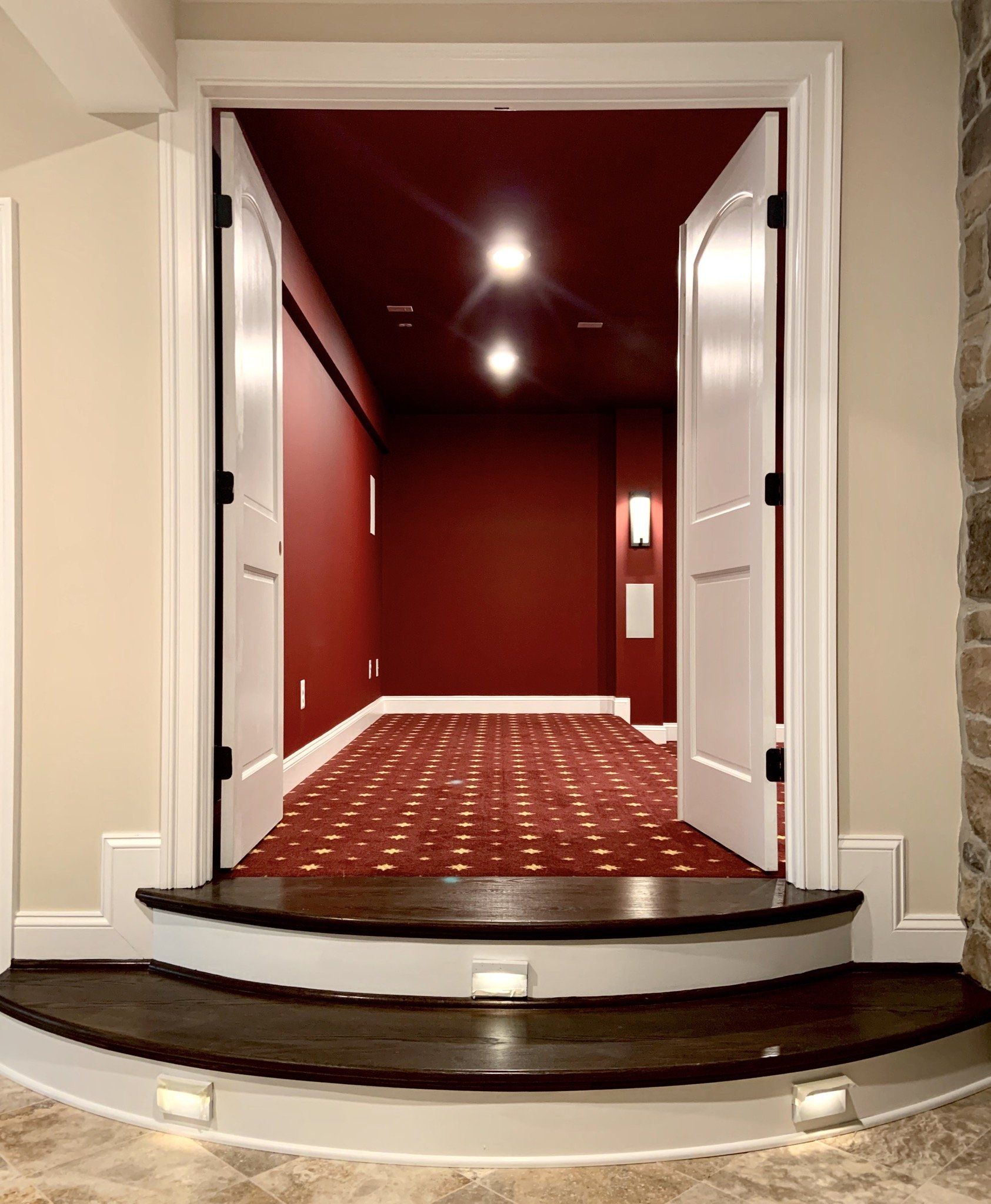 Open doorway leading into a dark red room with a carpeted floor, two steps down with built-in lights.