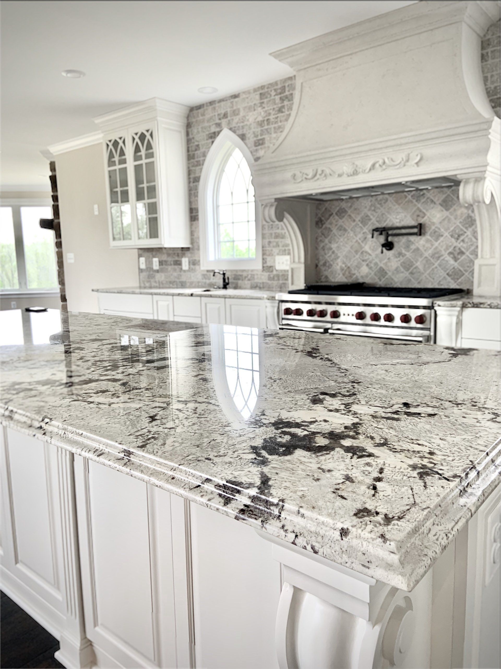 White kitchen with granite island, arched window, and range hood.