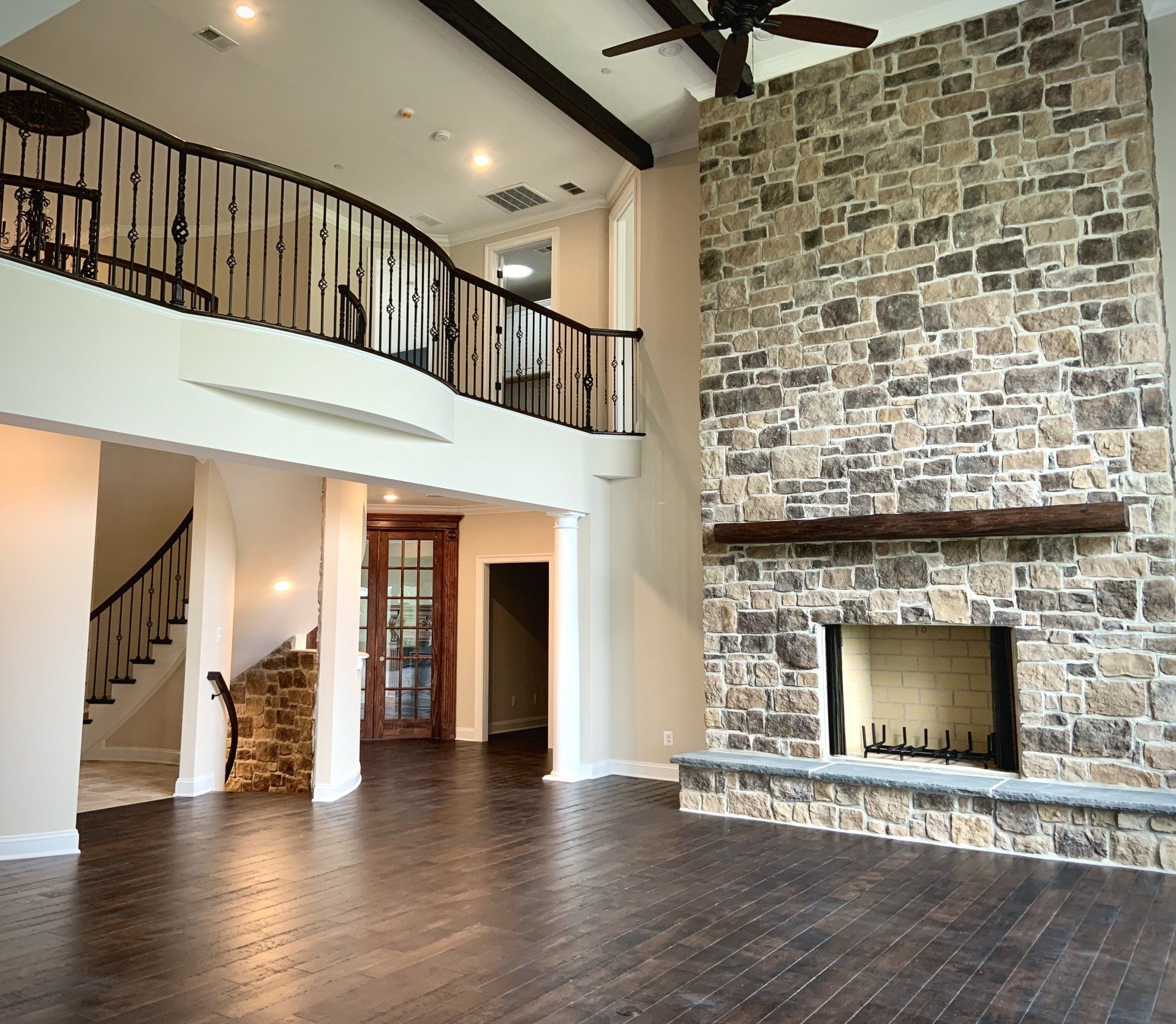 Large, open-concept living room with stone fireplace, dark wood floors, and balcony overlooking the space.