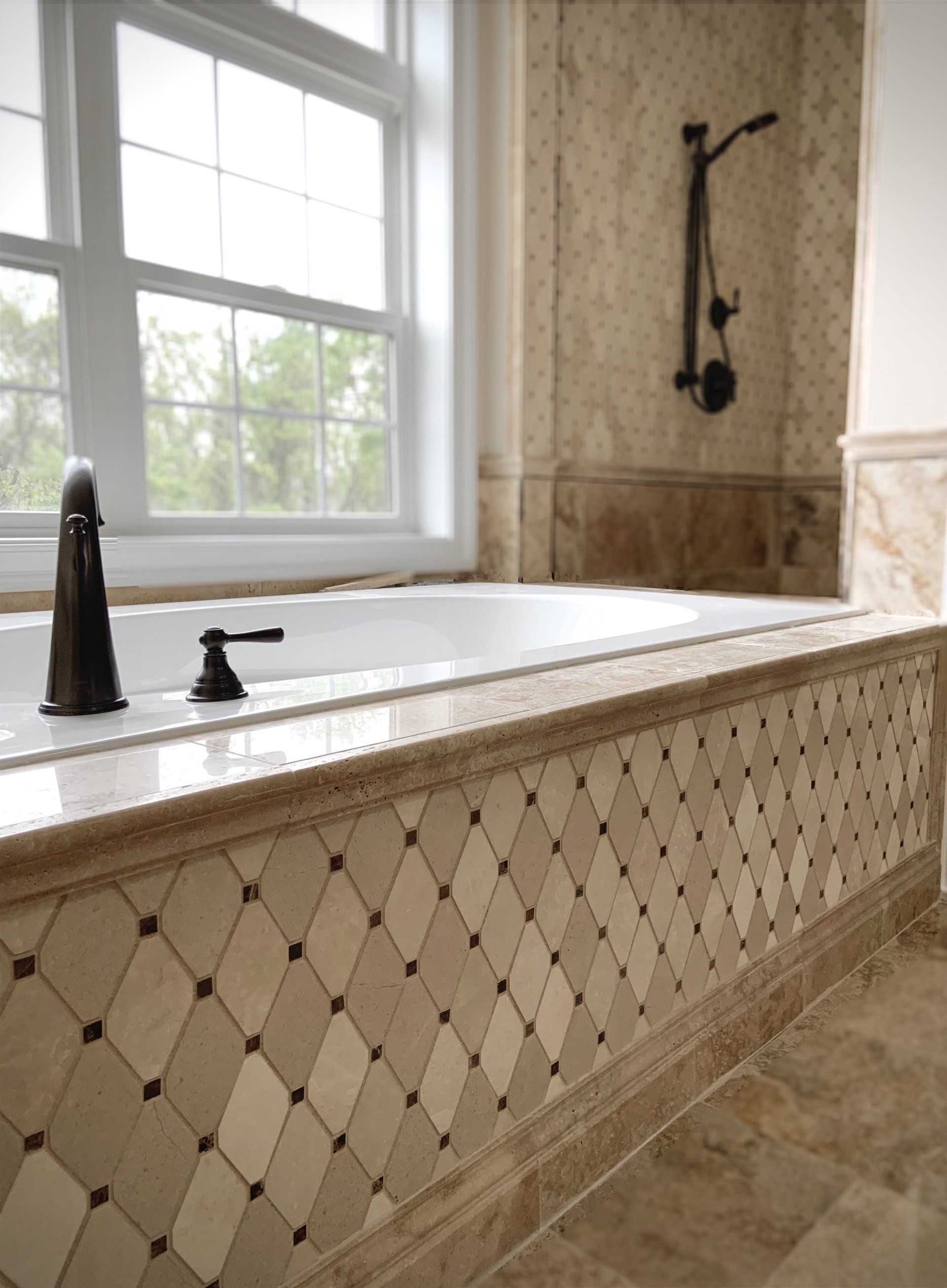 Bathroom with a tiled bathtub surround featuring diamond-patterned beige and brown tiles, next to a window and shower.