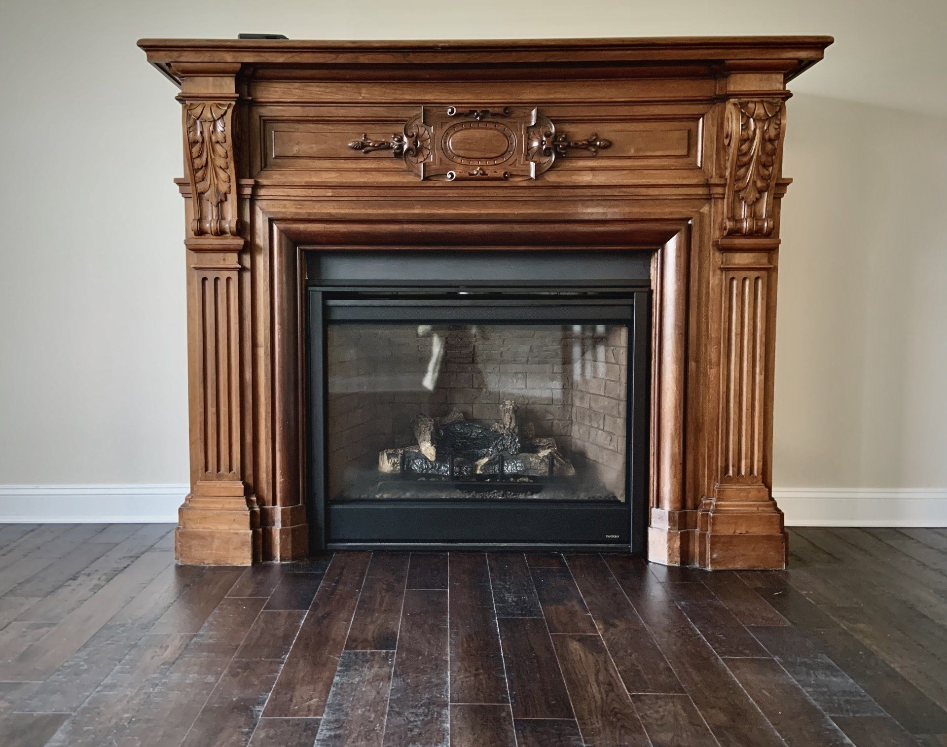 Ornate wooden fireplace with dark wood floor, against a light beige wall.
